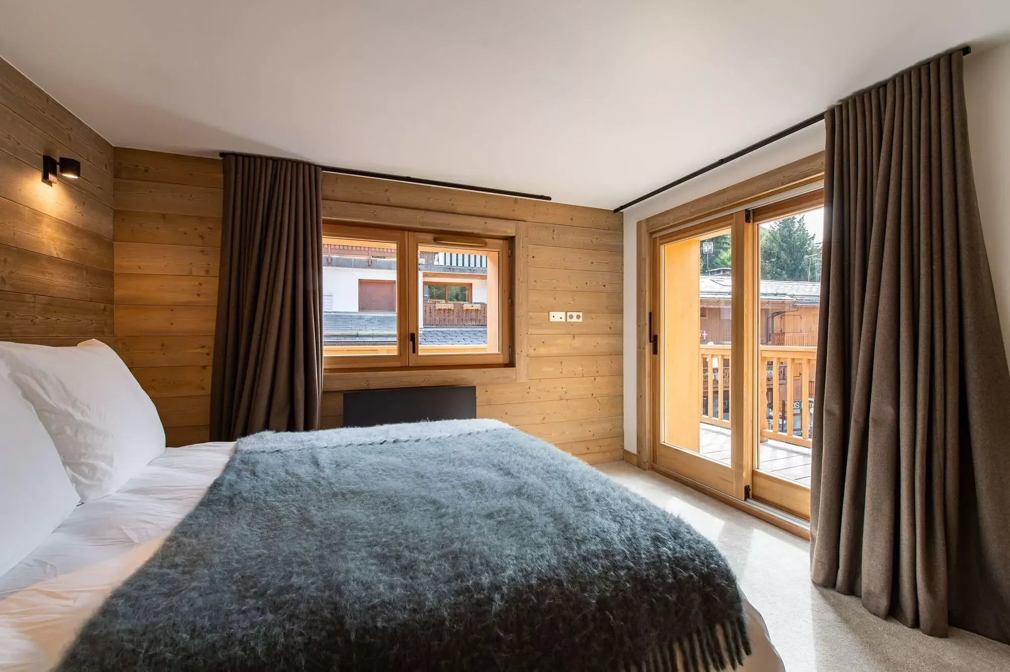 Large double bedroom with modern interior. Outside is a lovely decking area. Curtains are blackout and the bed is large with a grey throw.