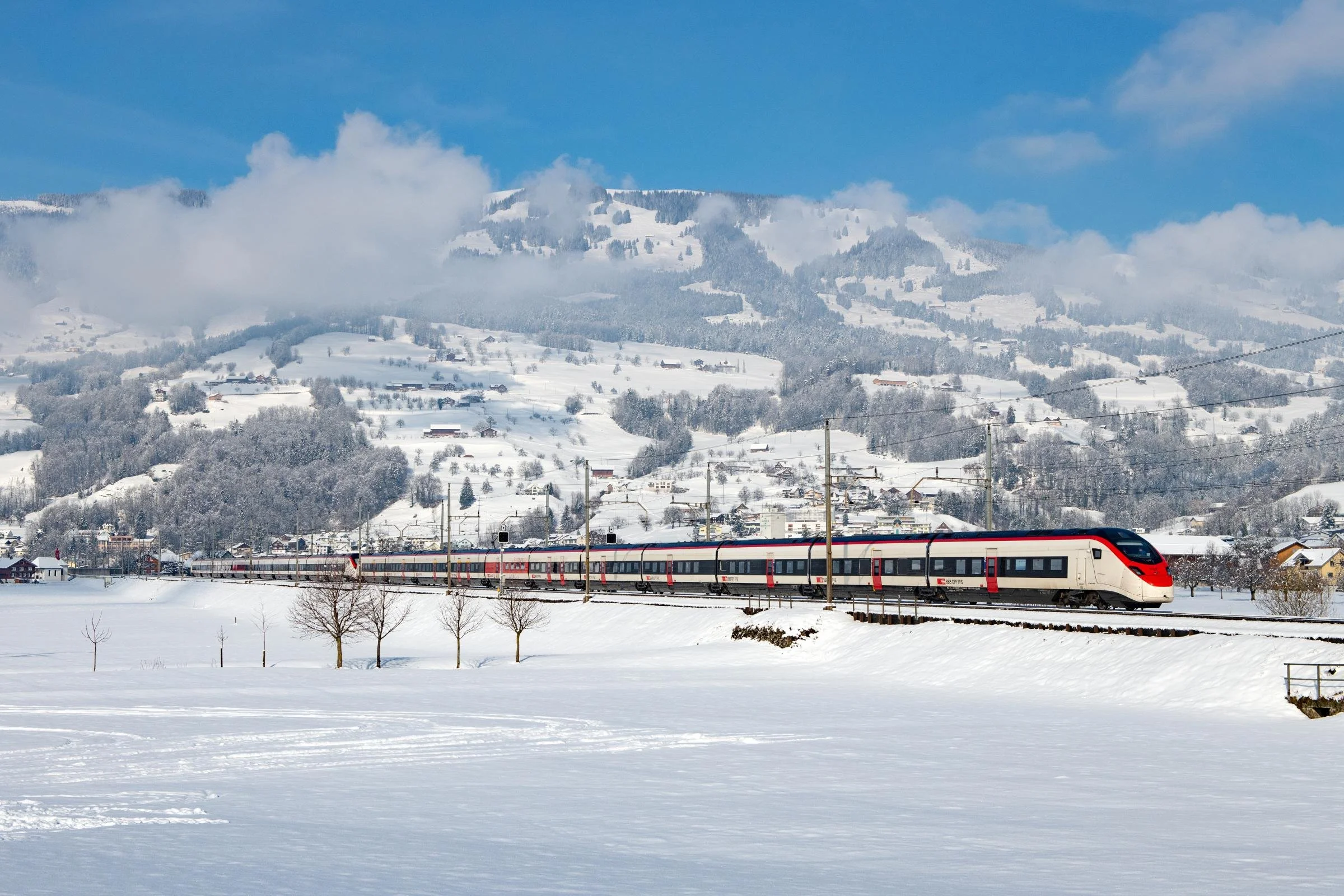 High-speed train soaring through the Swiss Alps with a mountainous backdrop. Windows lining the train allow passengers to admire the view.