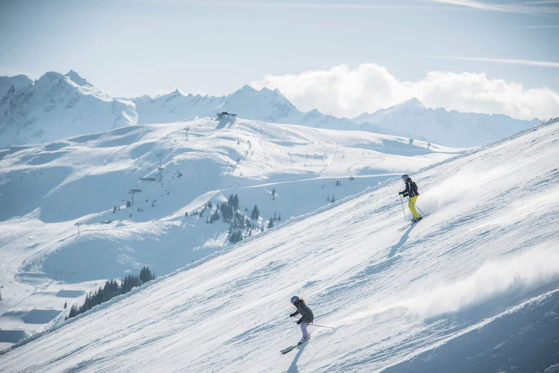 A couple skiing down the side of a mountain in sunny conditions.