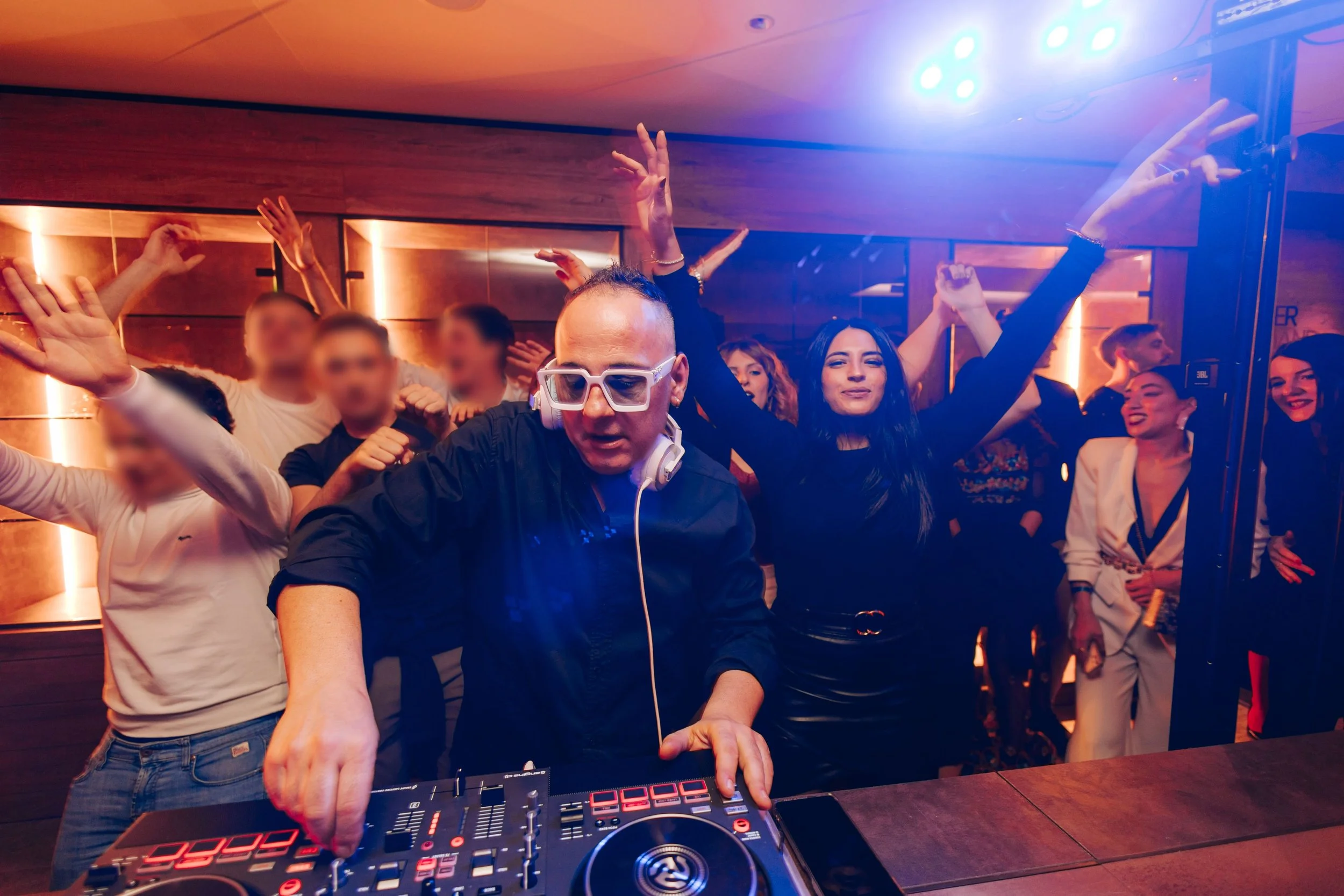 DJ performing at a lively party with a crowd dancing and enjoying music in a dimly lit club