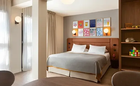 Double bedroom in a modern setting. Grey sheets with gold trim, modern furnishing and colourful tissue box.