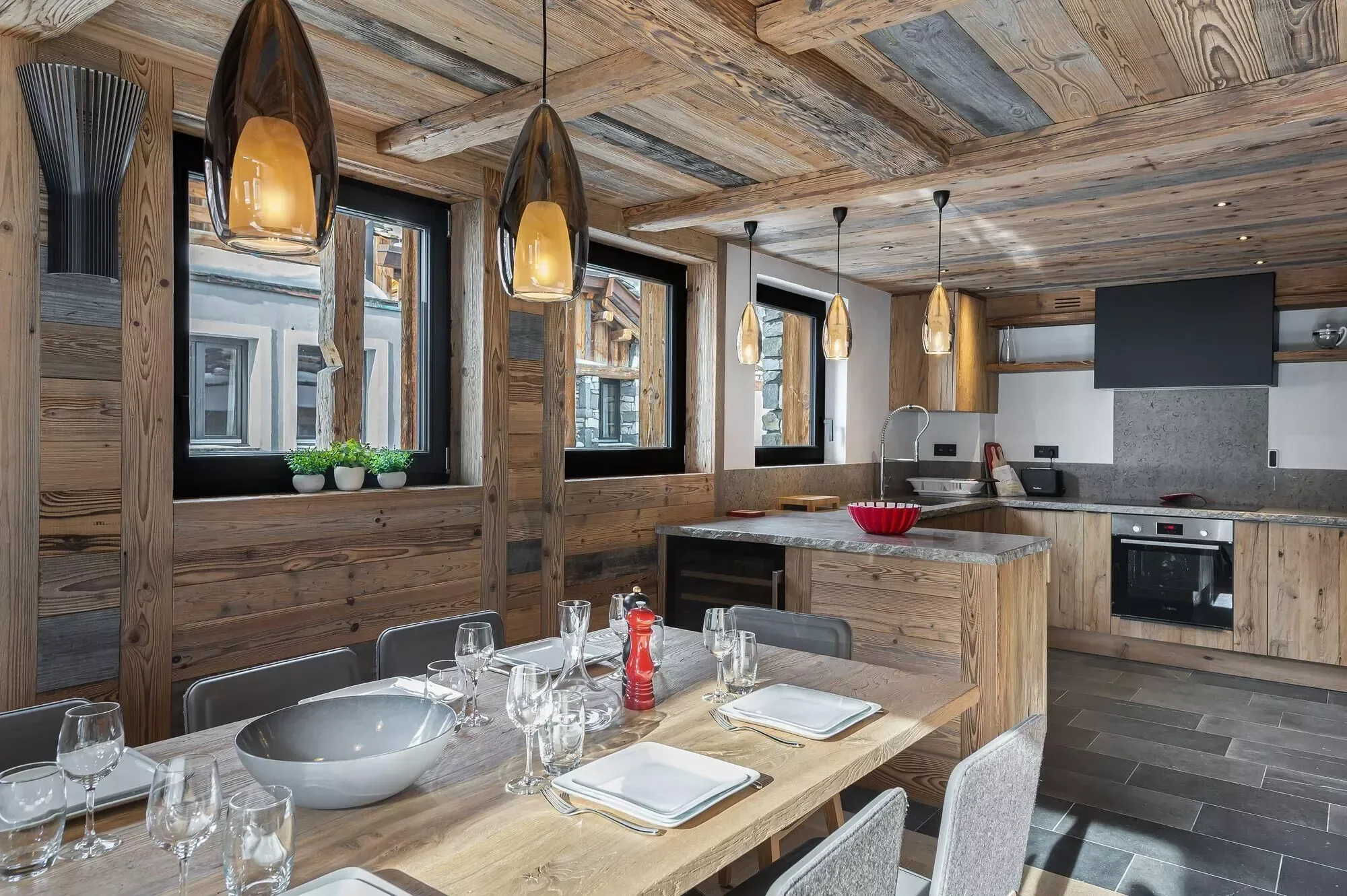 Modern dining table in the Chalet Angelus make this feel at home. Water drop style lights above the table help create a luxury atmosphere and a fully equipped kitchen behind for hosting.