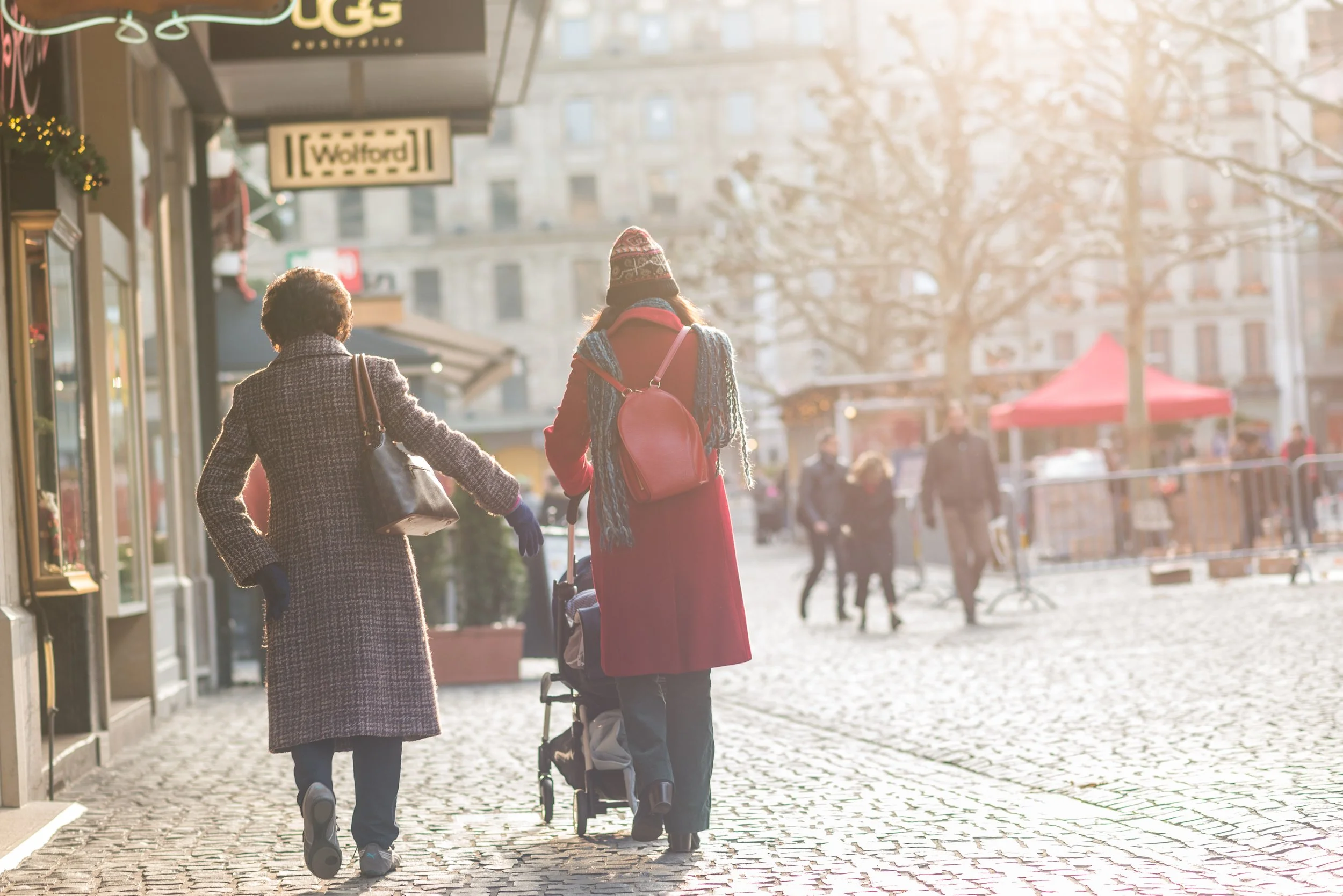 Christmas Market in Geneva with a lady in a red coat and another in a brown coat walking a pram along the streets of Geneva
