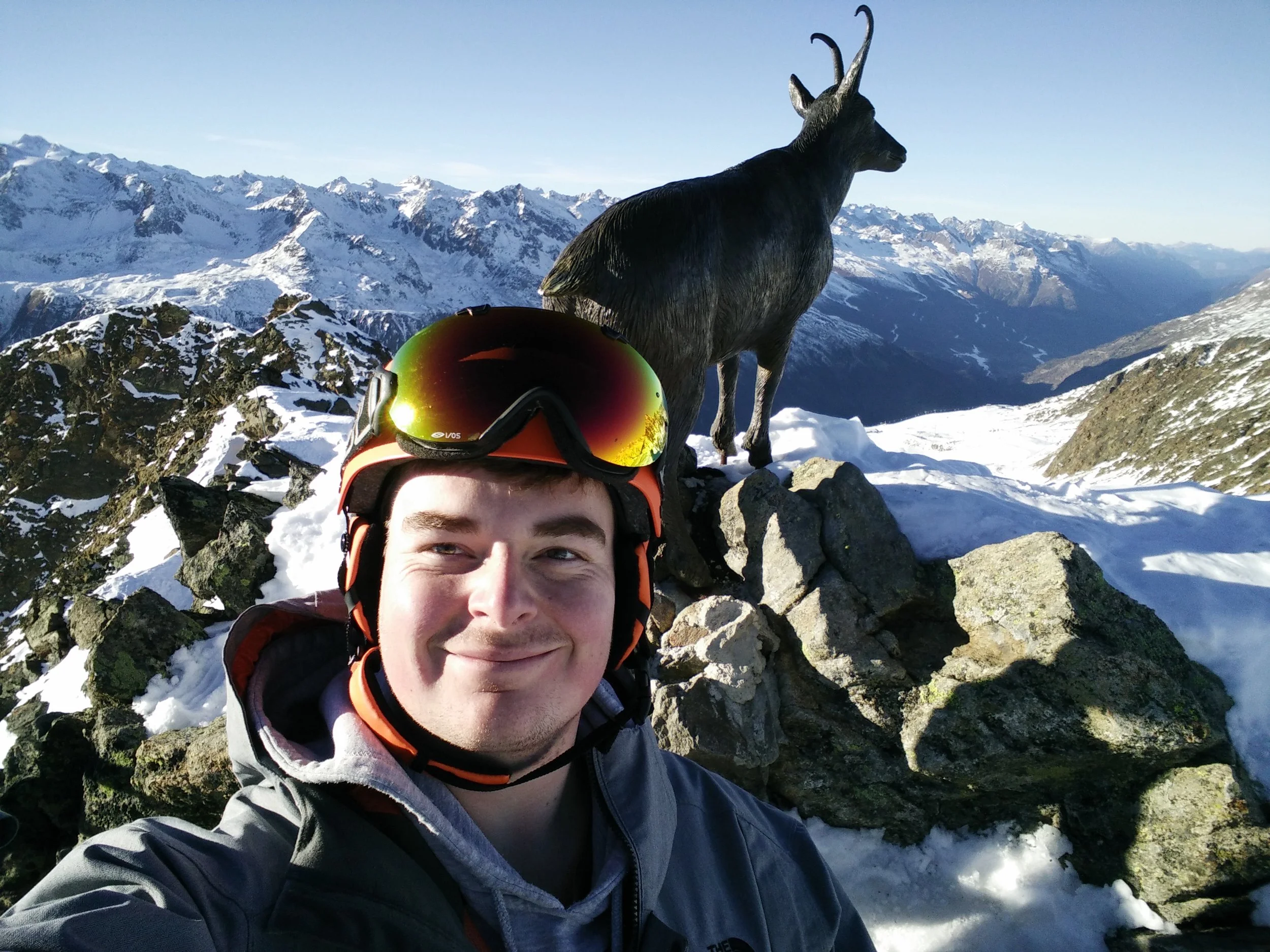 Peter Ledger standing oat the top of Obergurgl with a cast iron mountain goat behind and sunshine.