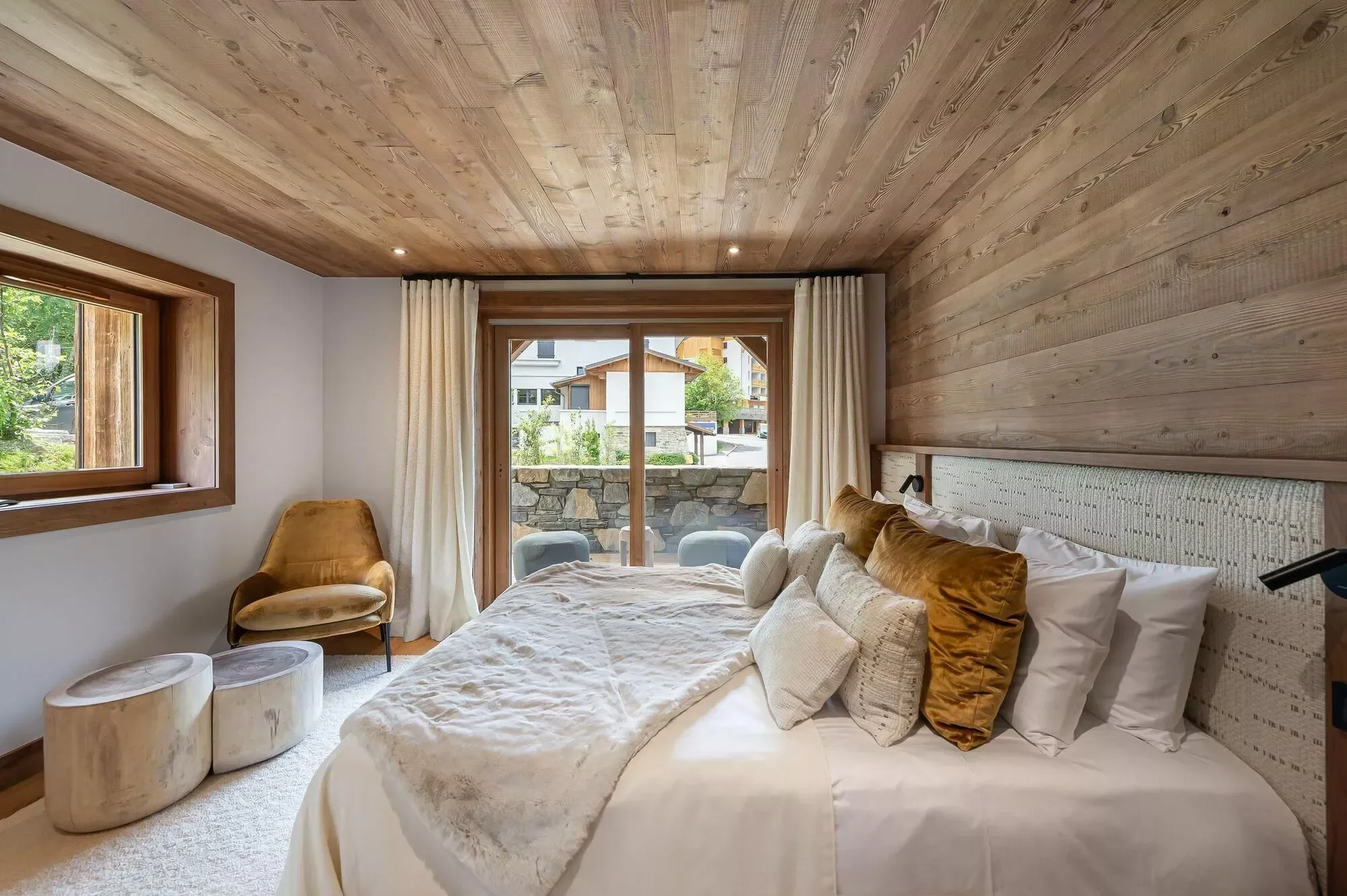 Indulgent double bedroom with plump cushions. Alpine wood ceiling and feature wall with fabric headboard. Plenty of space with small seating terrace.