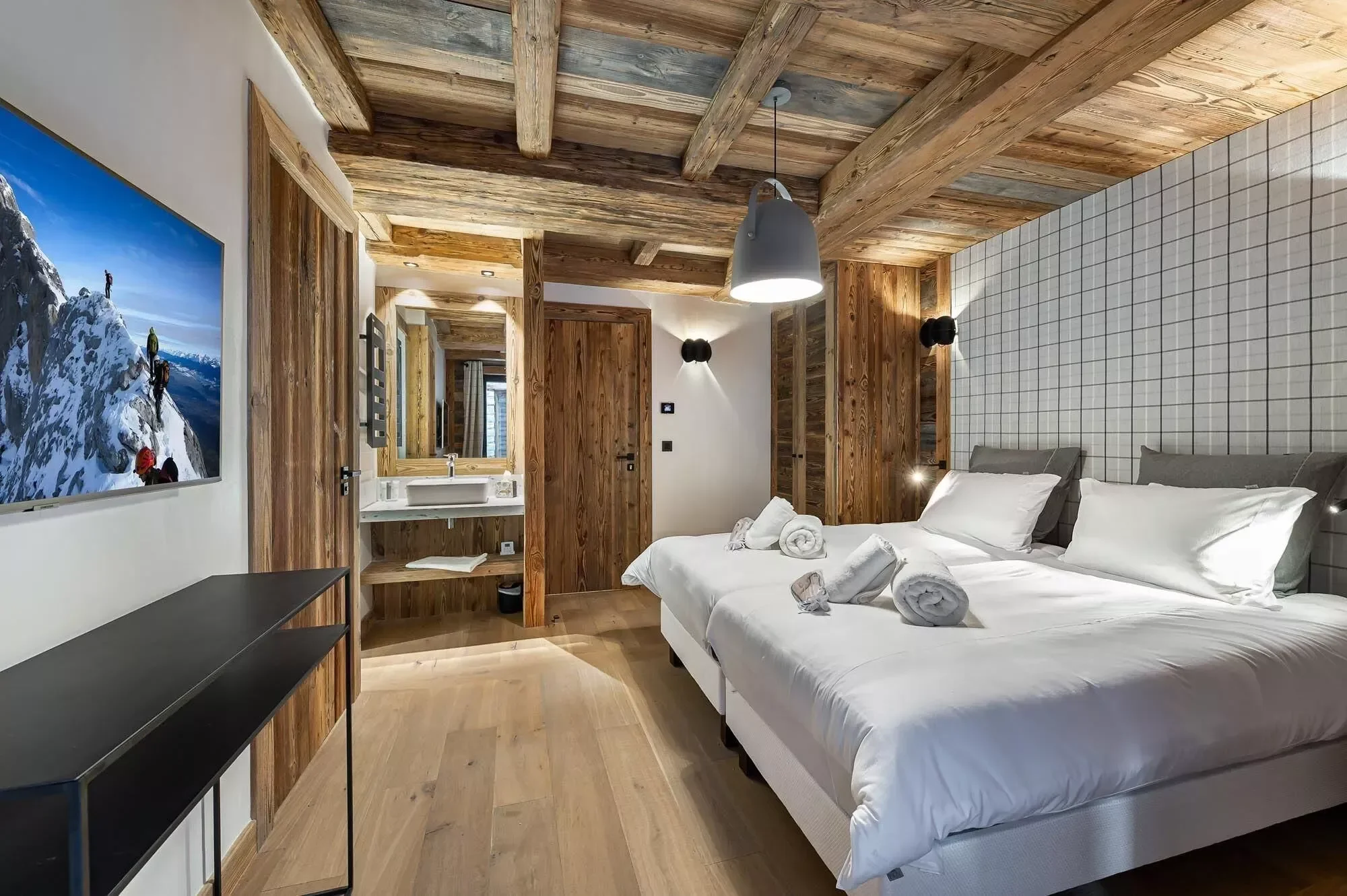 Lovely double bedroom or twin configuration with light grey modern interior. Plenty of wood to balance the alpine charm of this bedroom. Large TV on the wall and bathroom in the corner.