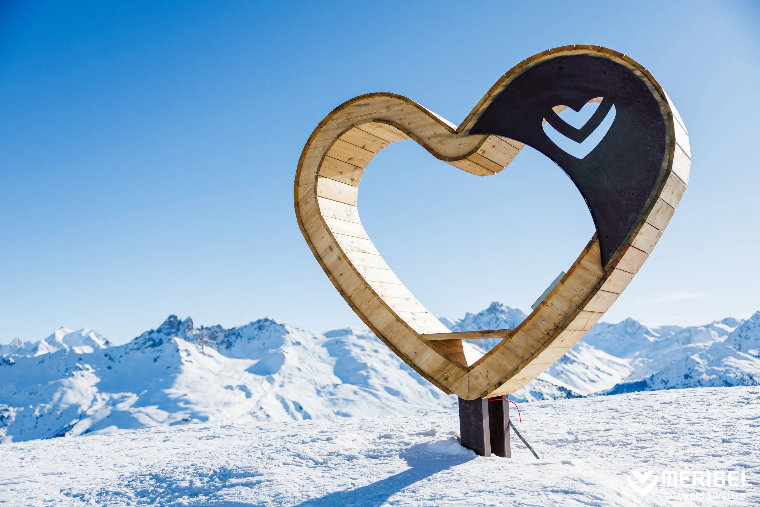 Wooden love heart shape at the top of the mountains in Meribel. Blue skies and mountain views as far as the eye can see.