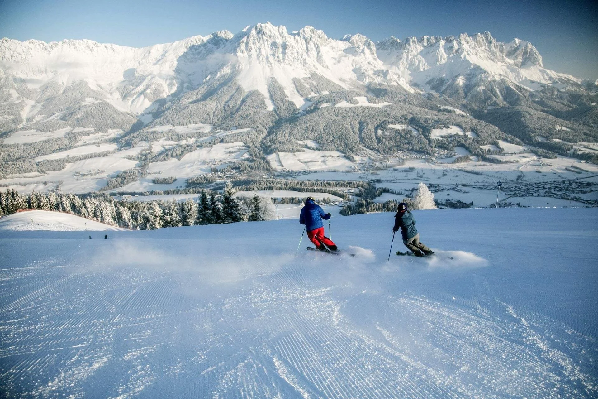 Two skiers going down the mountain on a fresh blue sky day and fresh snowfall.