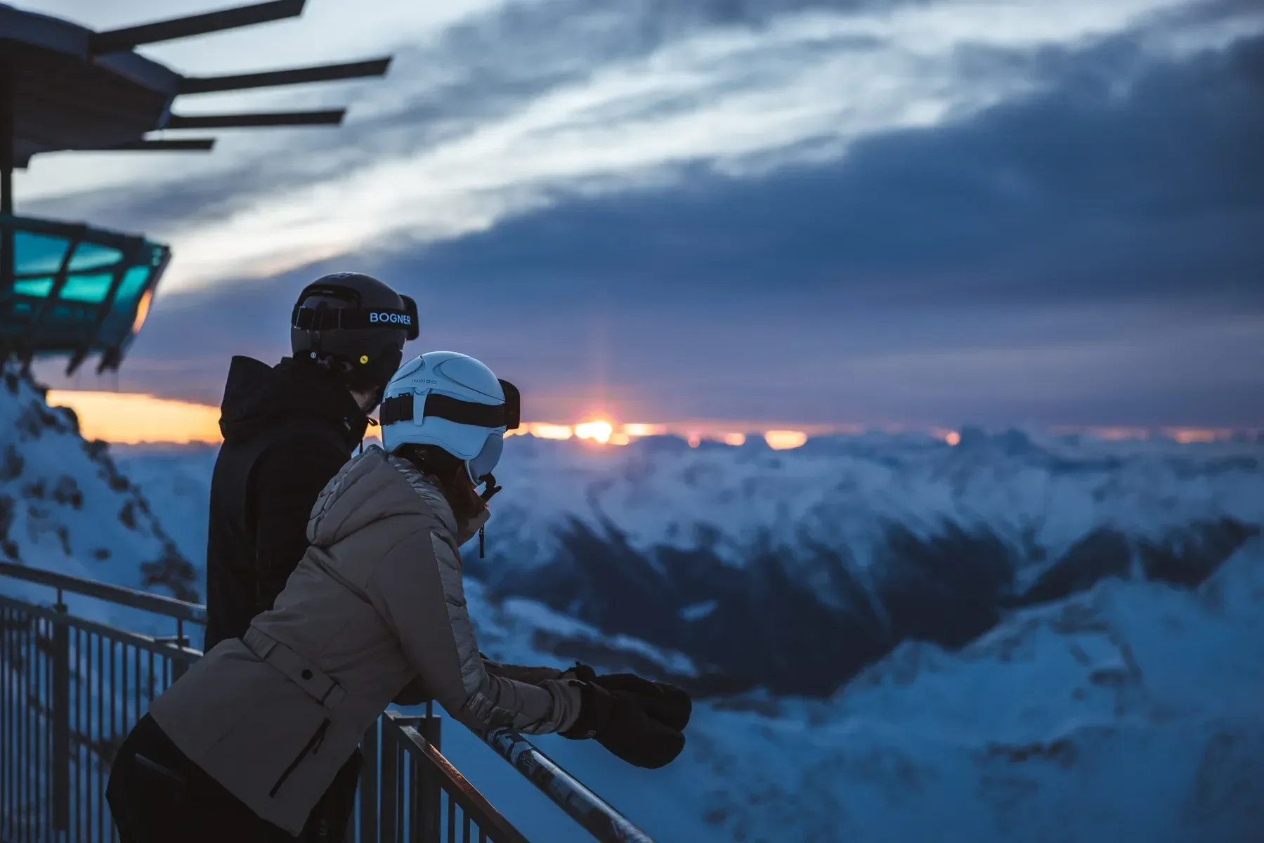 Sunset on top of Obergurgl. Two people look out over the mountains towards the setting sun.