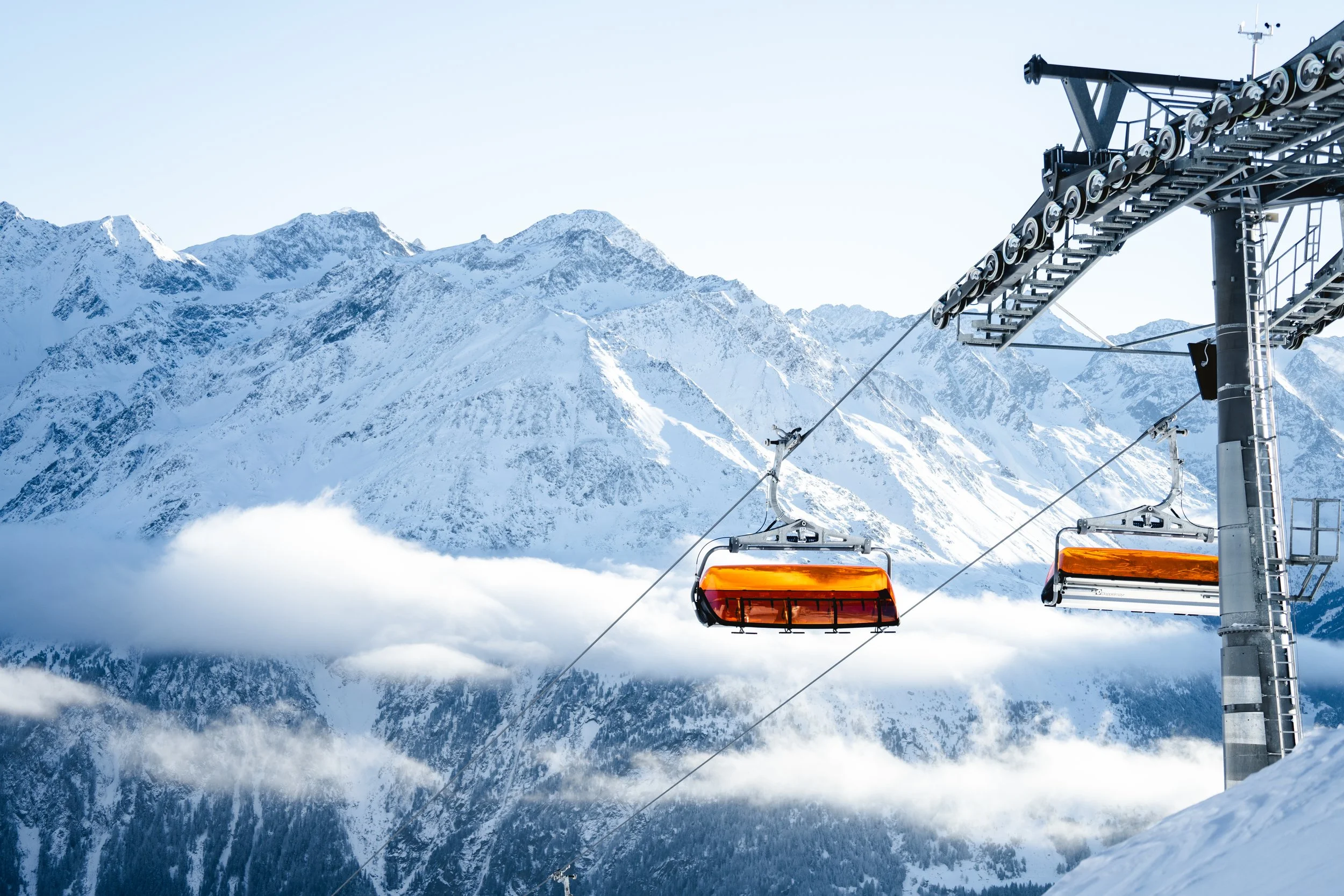 Snow-covered mountain range with ski lift chairs suspended in the air.