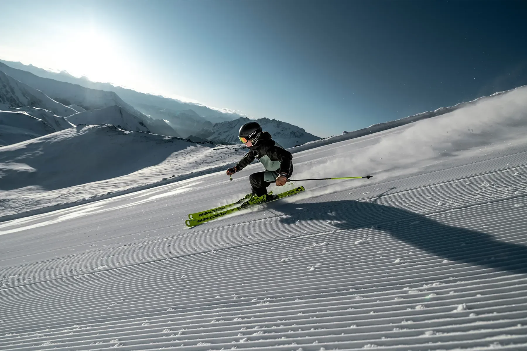 Advanced skier heading downhill at pace in a blue jacket, green skis and fresh blue sky conditions