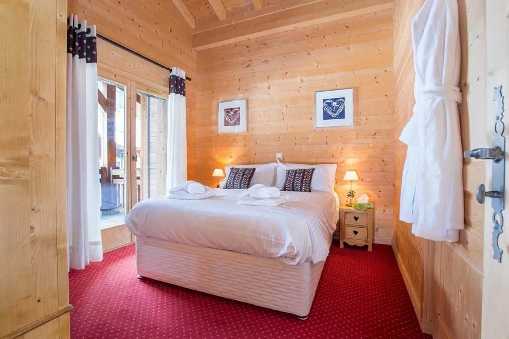 Double bed with red carpet, pine wooden walls and white furnishings.