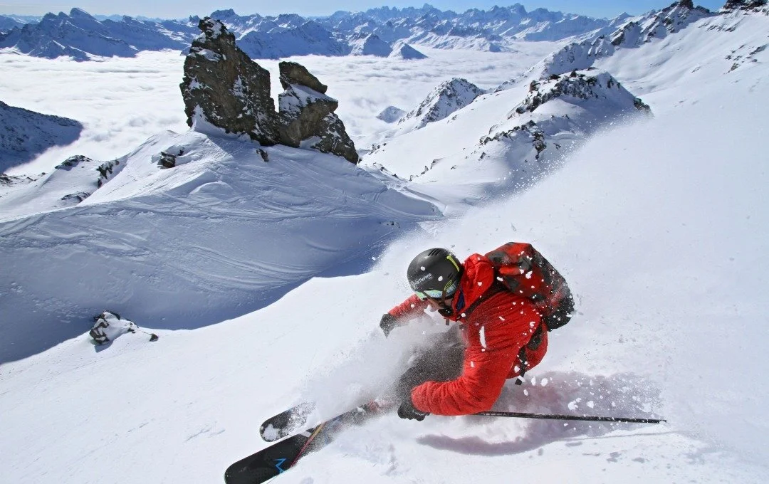 Advanced big mountain skier heading down the side of the mountain in Val Thorens. Red jacket, black helmet and powder skis.