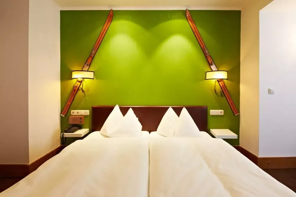 Austrian twin bedroom with a green backwall containing two sets of ski lights for creative design. White plush interior and a modern Tirolean style.