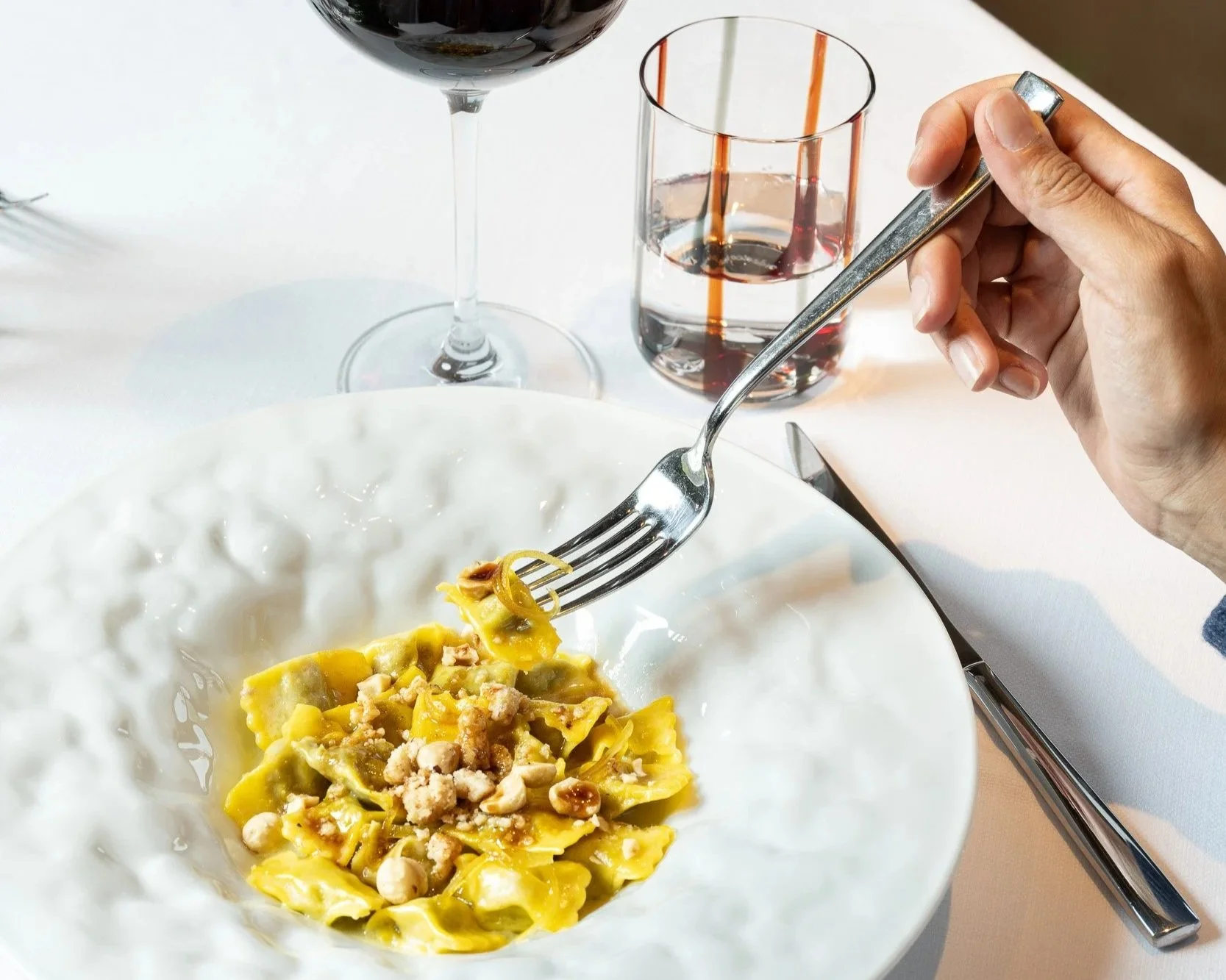 Pasta course. Filled pasta with fresh nuts, a lovely white pasta bowl for service and a glass of red wine.