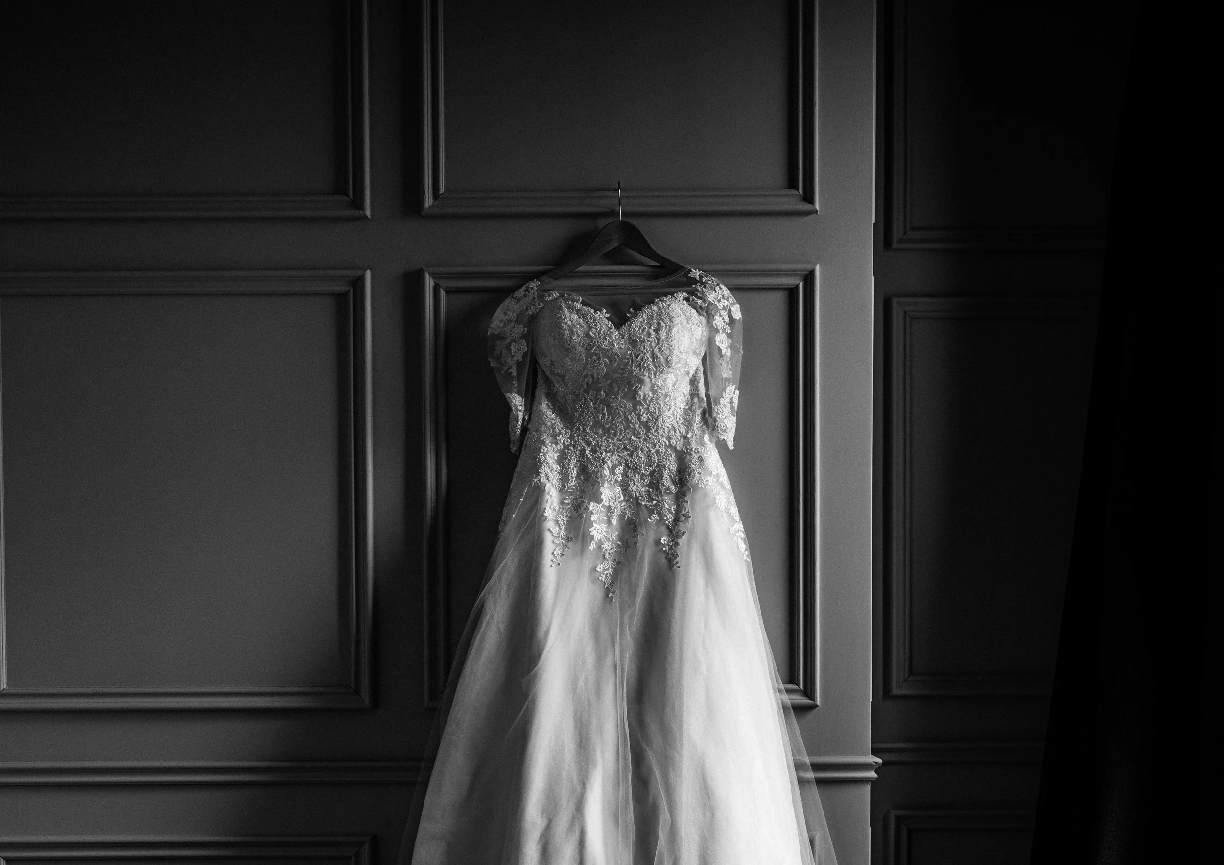 A wedding dress hanging on a hanger against a dark paneled wall.