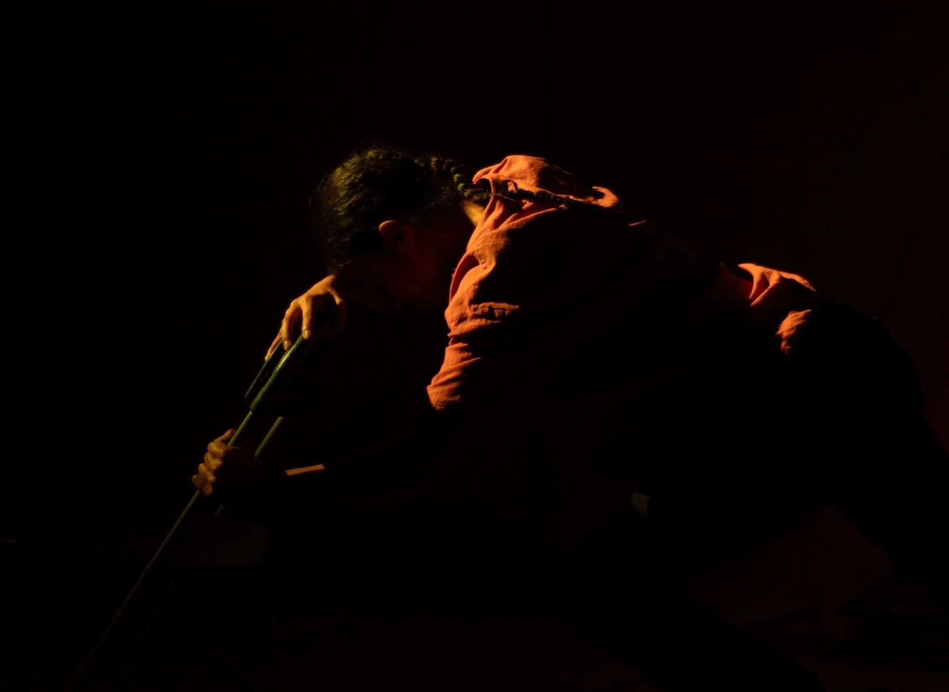 Person crouching in low light, holding crutches, with their head bowed and face close to their knee, in a dark setting.