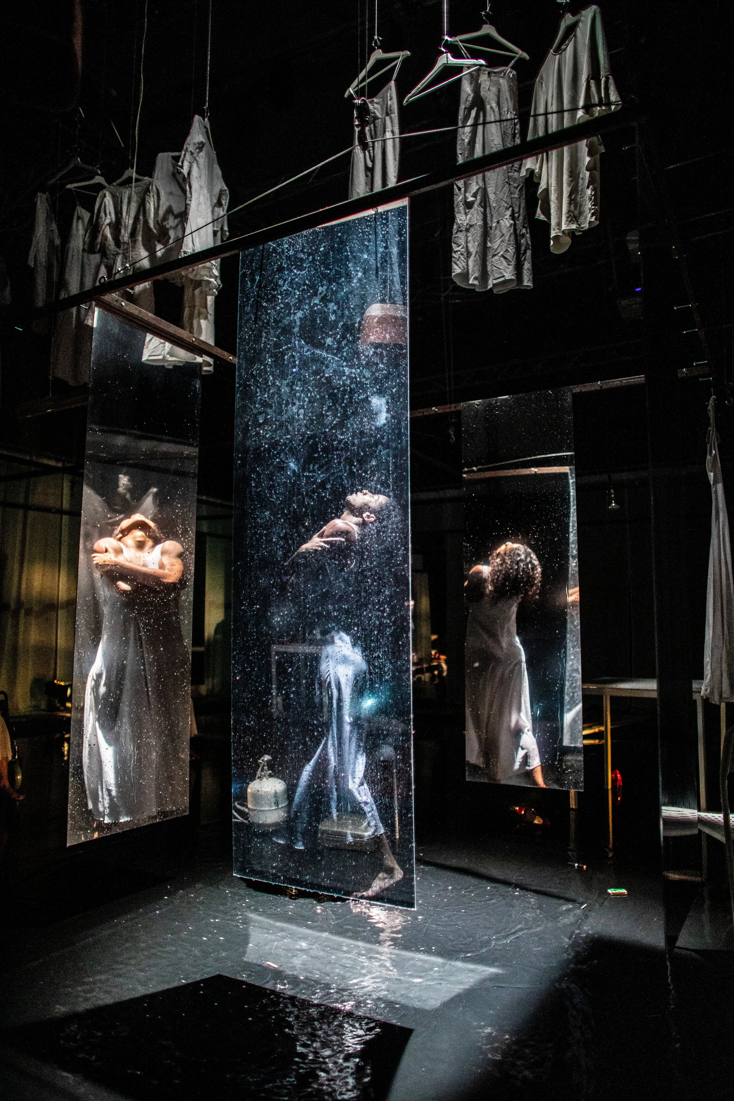 Installation with hanging mirrors that reflect a woman in a dress, with clothes hanging above.
