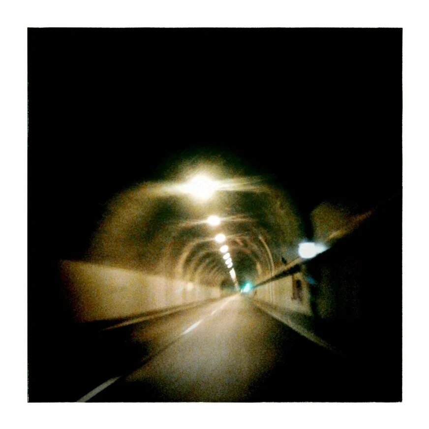 View inside a dark tunnel with overhead lights and a road extending into the distance.