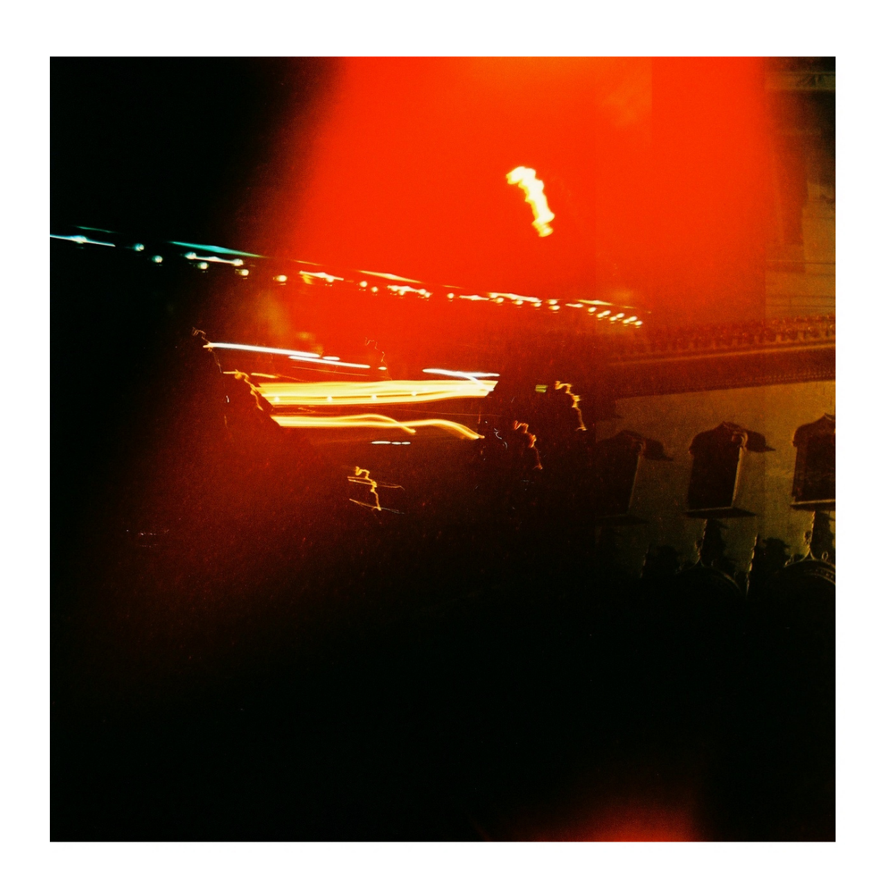 Blurry abstract night scene with streaks of orange, yellow, and white lights and silhouettes of people or objects in the foreground.