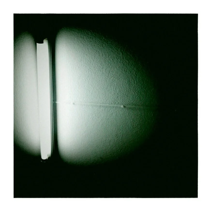 A diagonal fluorescent light fixture mounted on a textured wall, casting a circular glow around it.