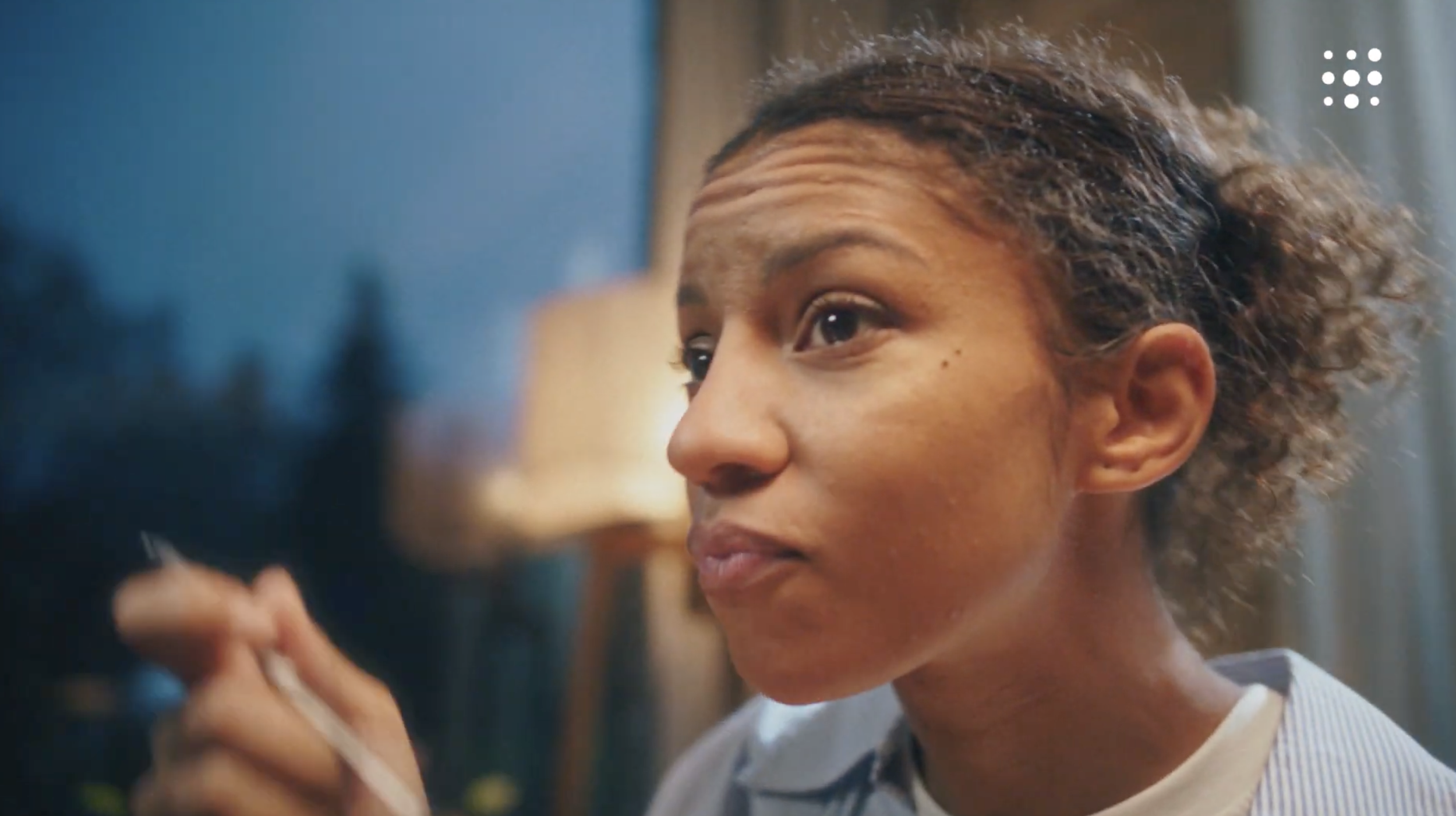 Close-up of a woman with curly hair and light skin looking to the side, with a blurred background.