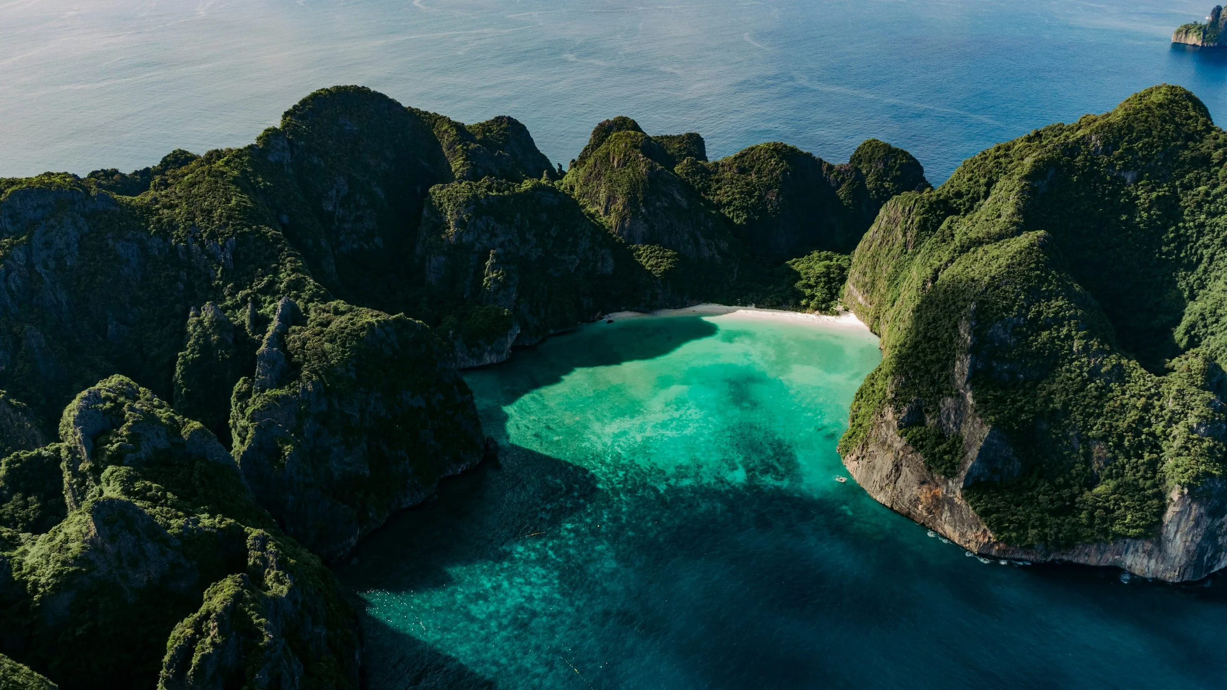 Aerial view of a tropical bay surrounded by lush green cliffs with turquoise water inside.