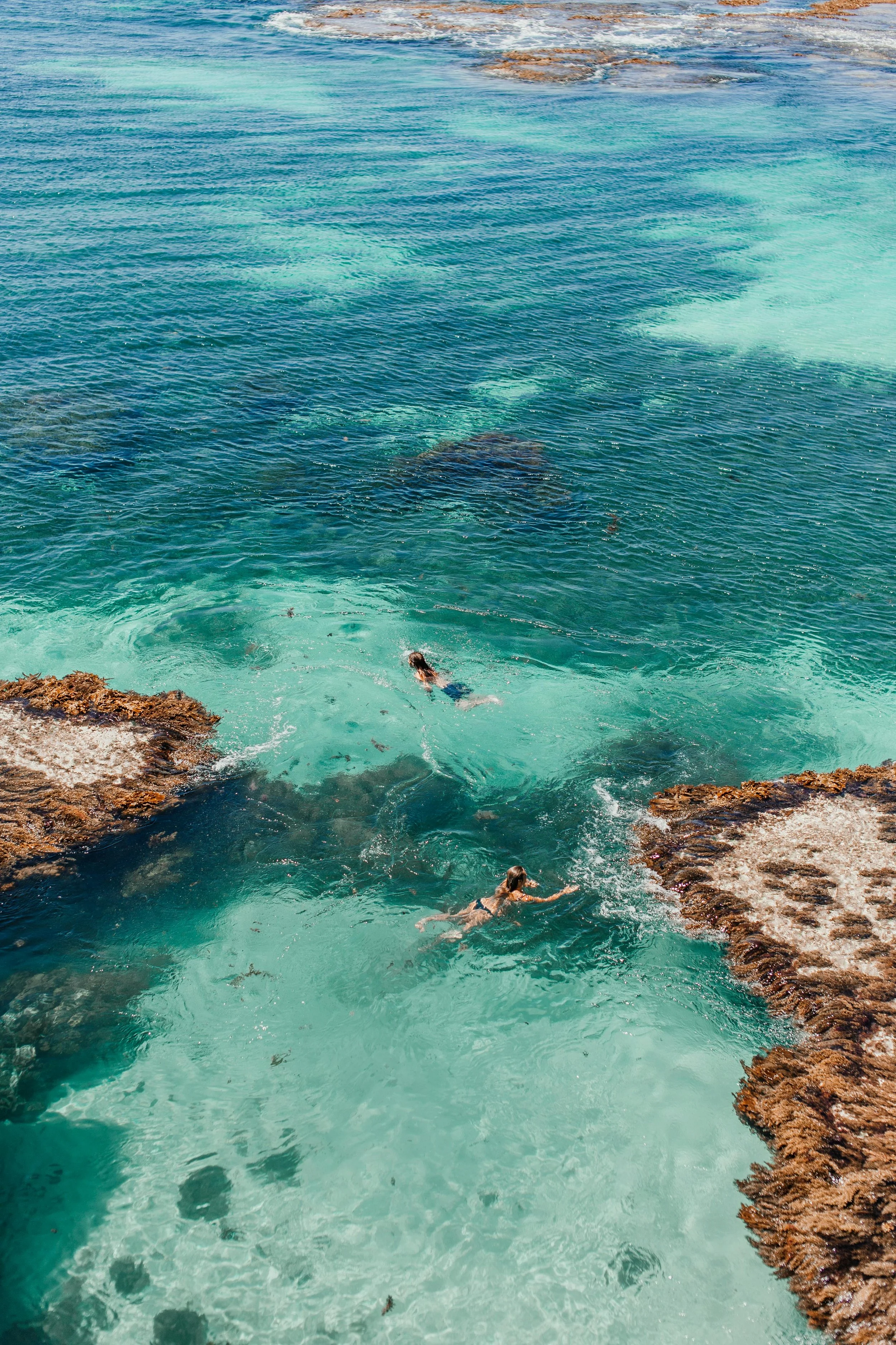People swimming in clear, turquoise water near rocky shoreline.