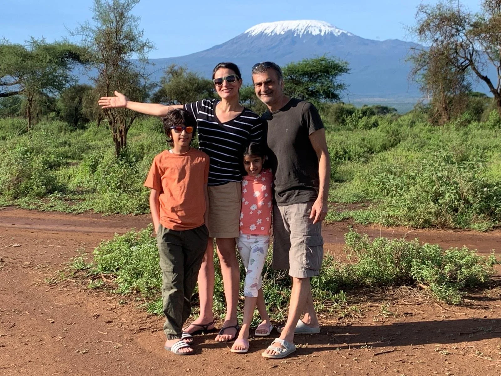 Family of four standing outdoors with Mount Kilimanjaro in the background. Children wear casual clothes, and adults are smiling.
