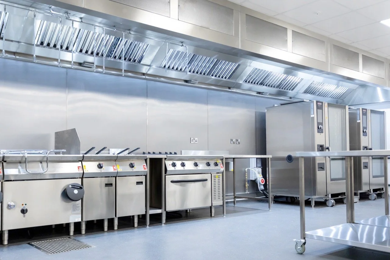 Commercial kitchen with stainless steel appliances including stoves, ovens, and ventilation hoods.