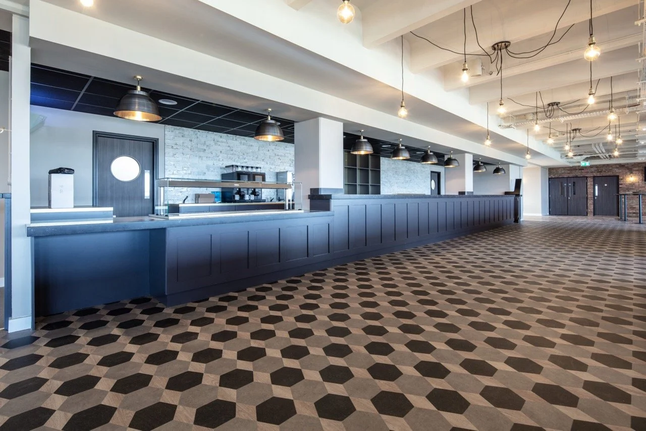 Large bar area with a midnight-blue panelled bar and black, grey and cream tiled floor.