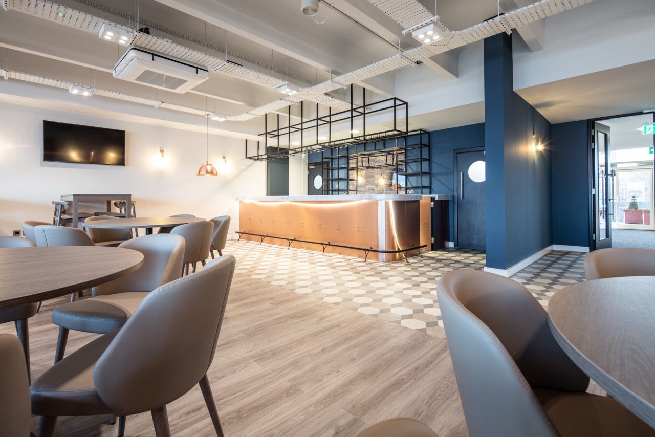 Bronze metal bar with black chrome light fittings in a midnight-blue walled room.