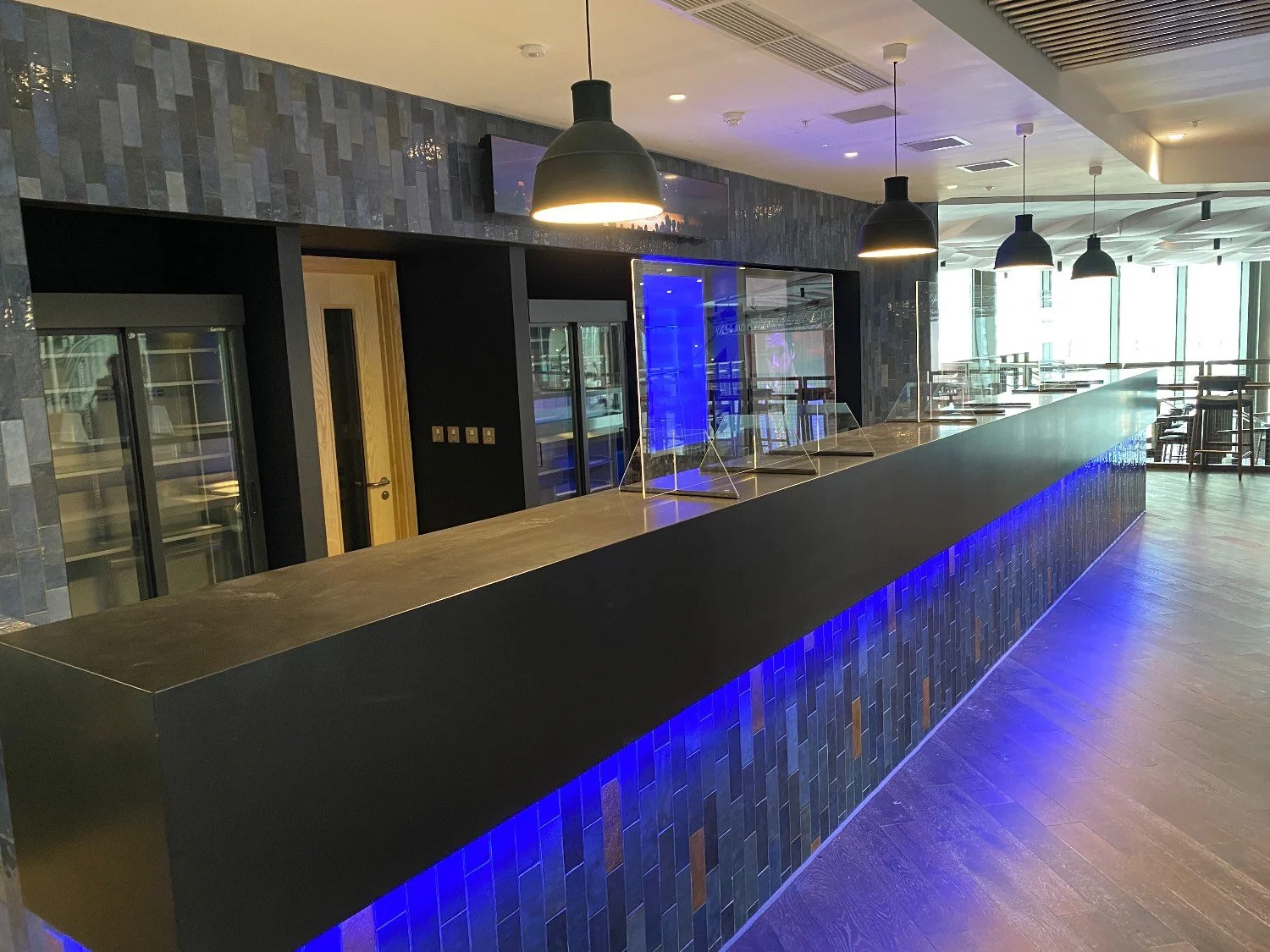 A dark bar area with a walnut coloured bar and blue strobe  lighting coming out the bottom of the bar.