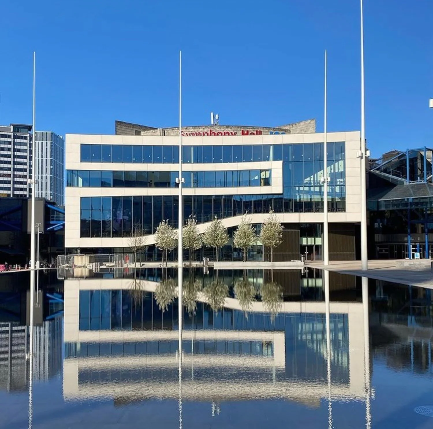 Modern, stylish building with flagpoles in front set behind a blue lake - the lake shows the reflection of the building.