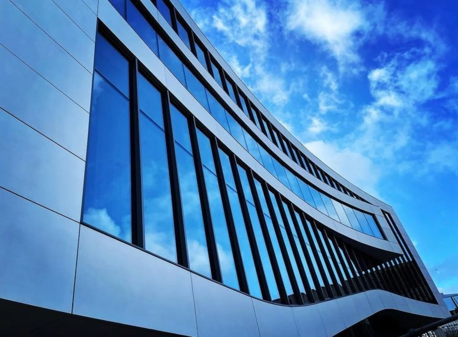Closeup of a curved modern building with bright blue sky behind.