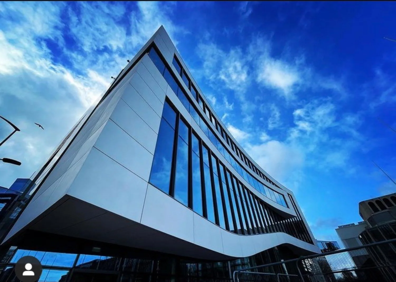 Closeup of a curved modern building with bright blue sky behind.