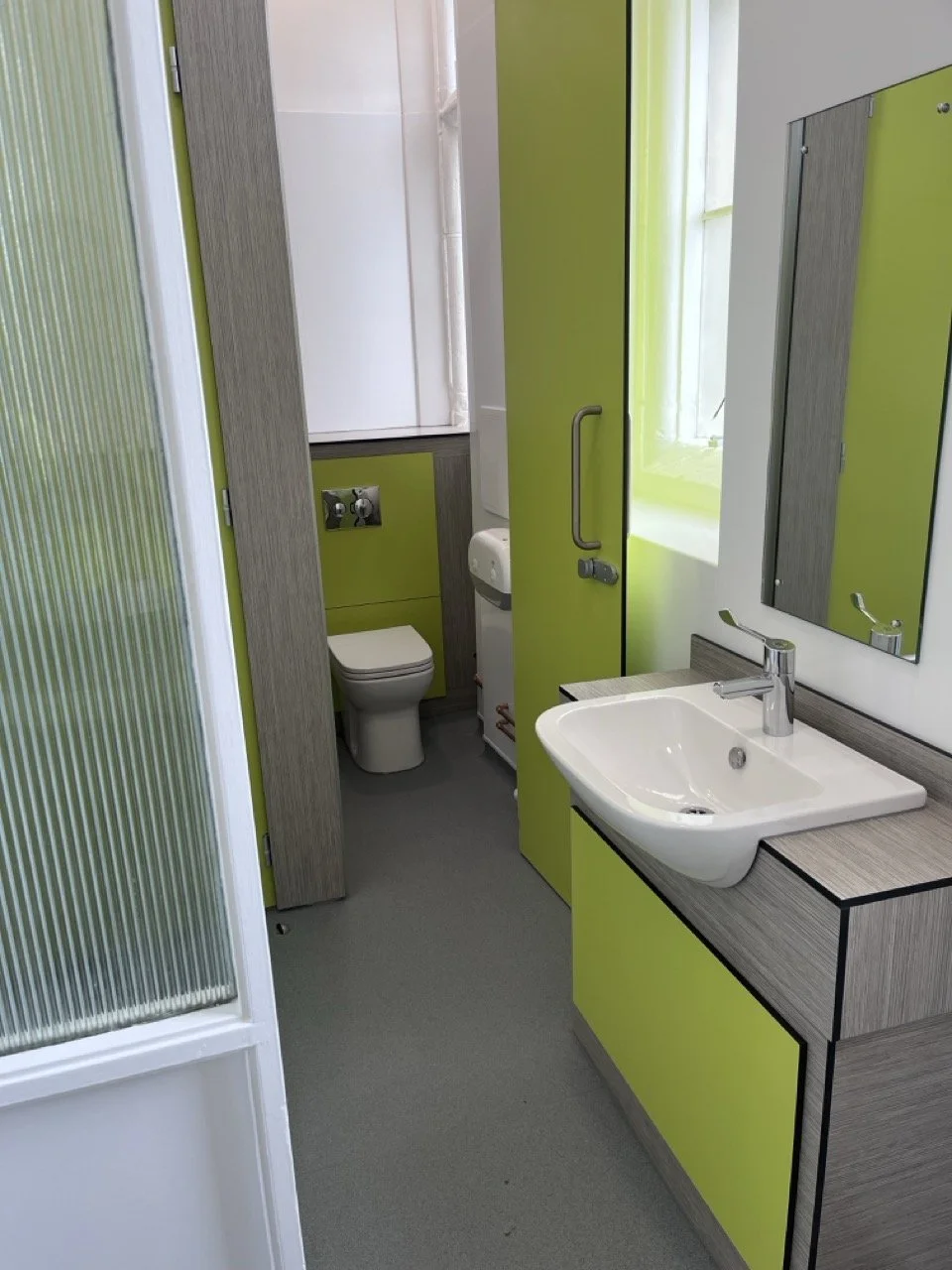 Looking into a lime green walled toilet area with a toilet cubicle and a white basin.
