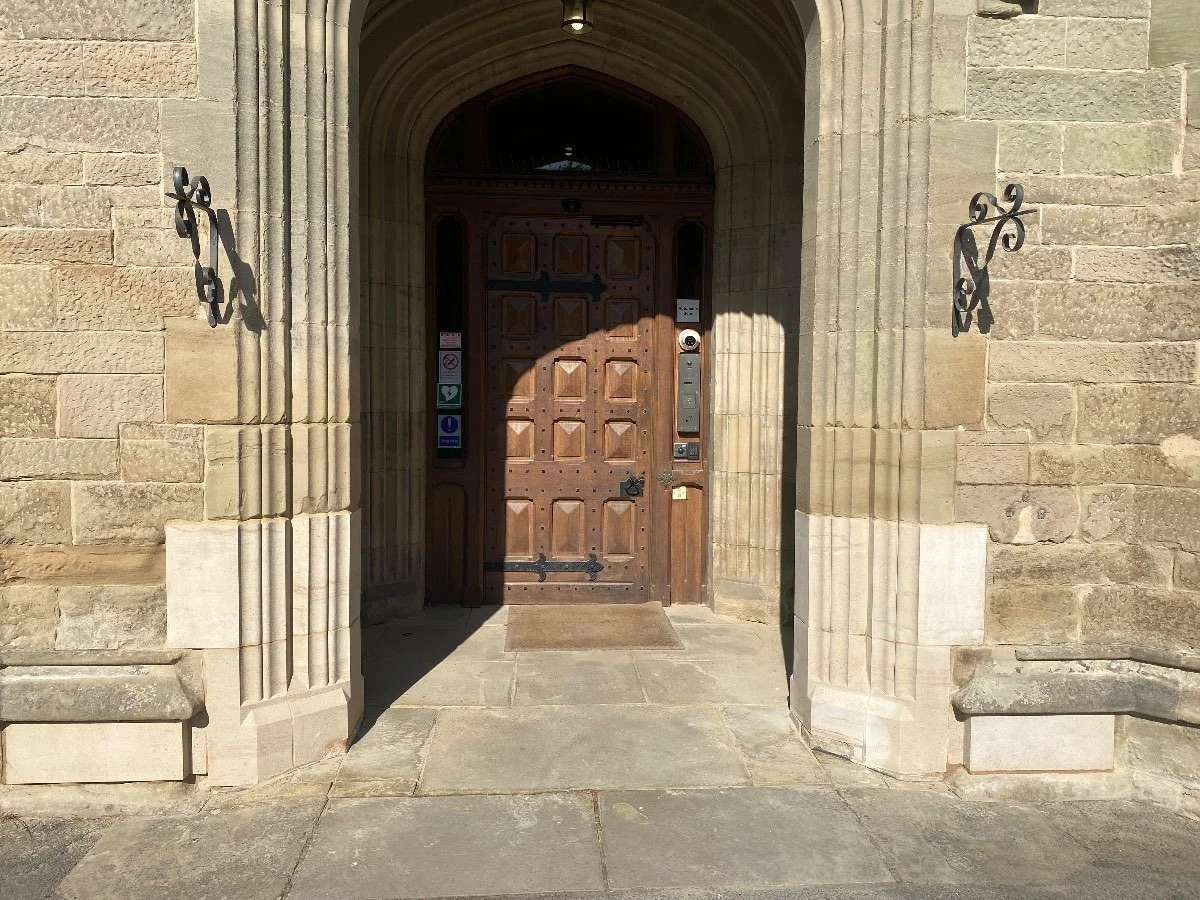 Old wooden doorway with black chrome hardware, sitting in a stone archway.