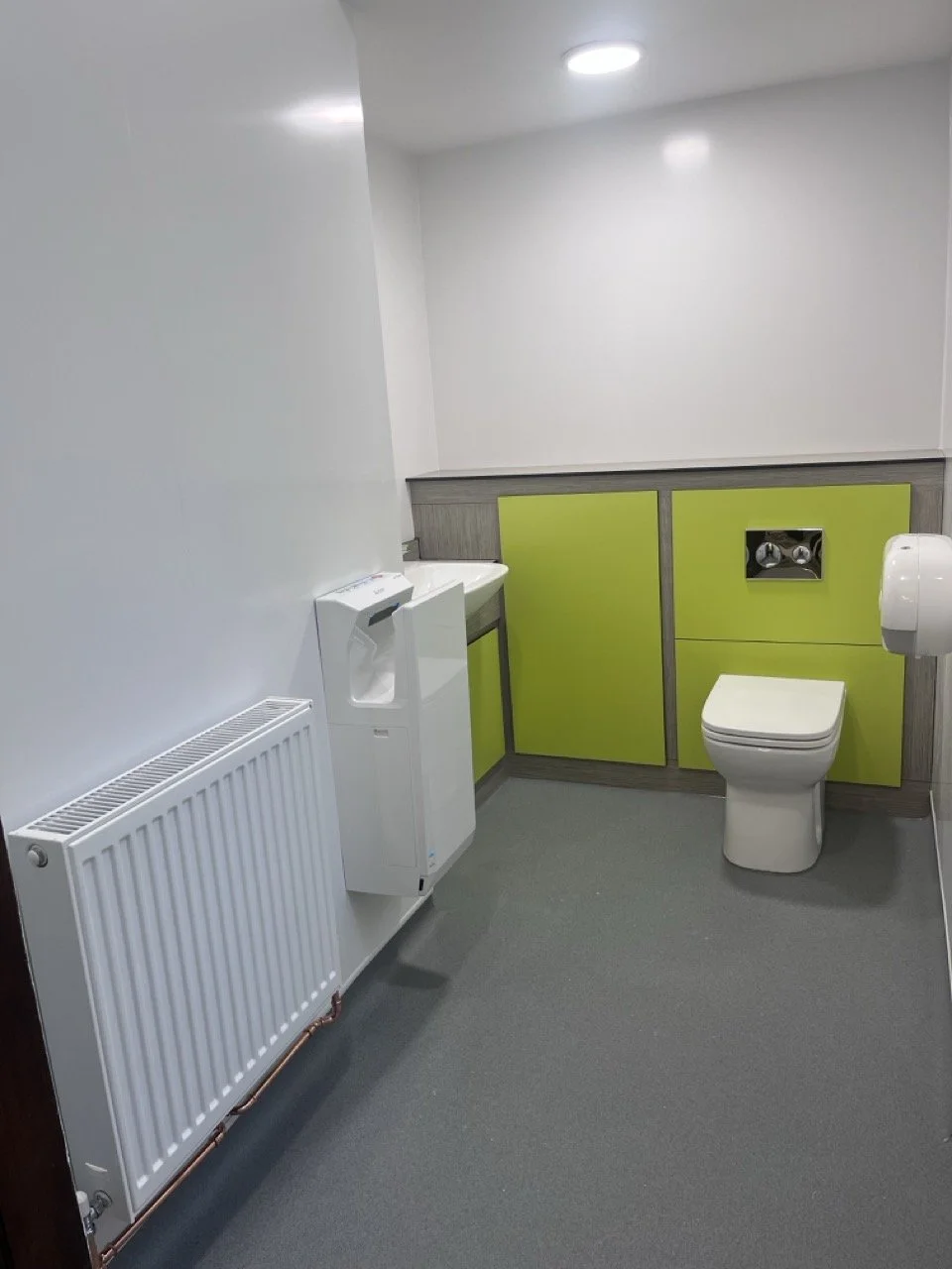 Large single toilet with white walls, white toilet and sink and lime green panelling.
