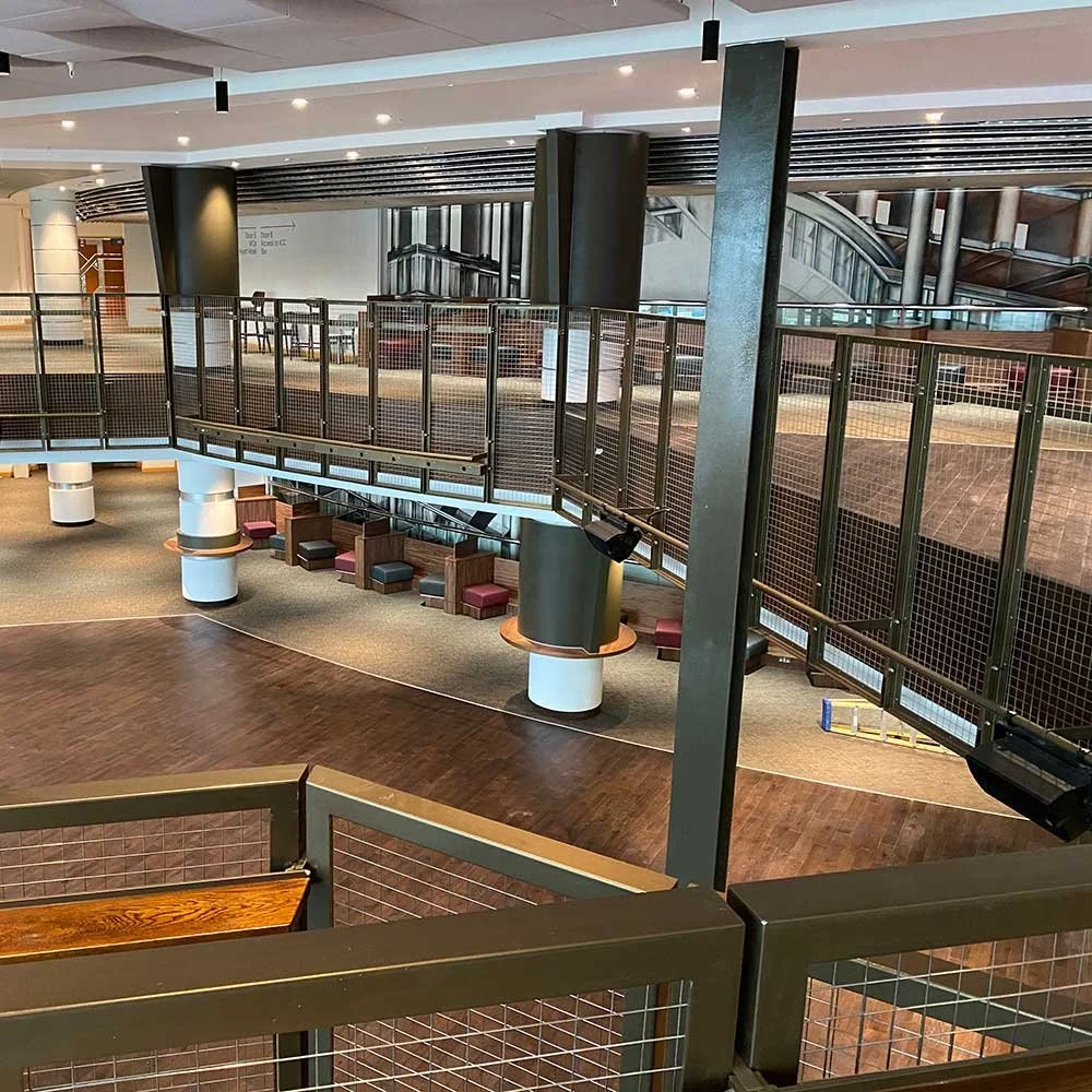 Empty multi-level indoor space with a walkway, seating area with chairs, and modern architectural elements.