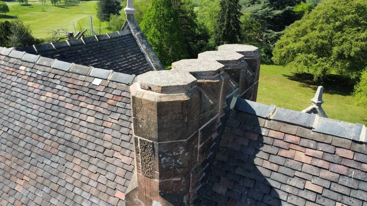 Closeup of a row of four chimneys on an old Scottish house. In the background are lush manicured gardens.