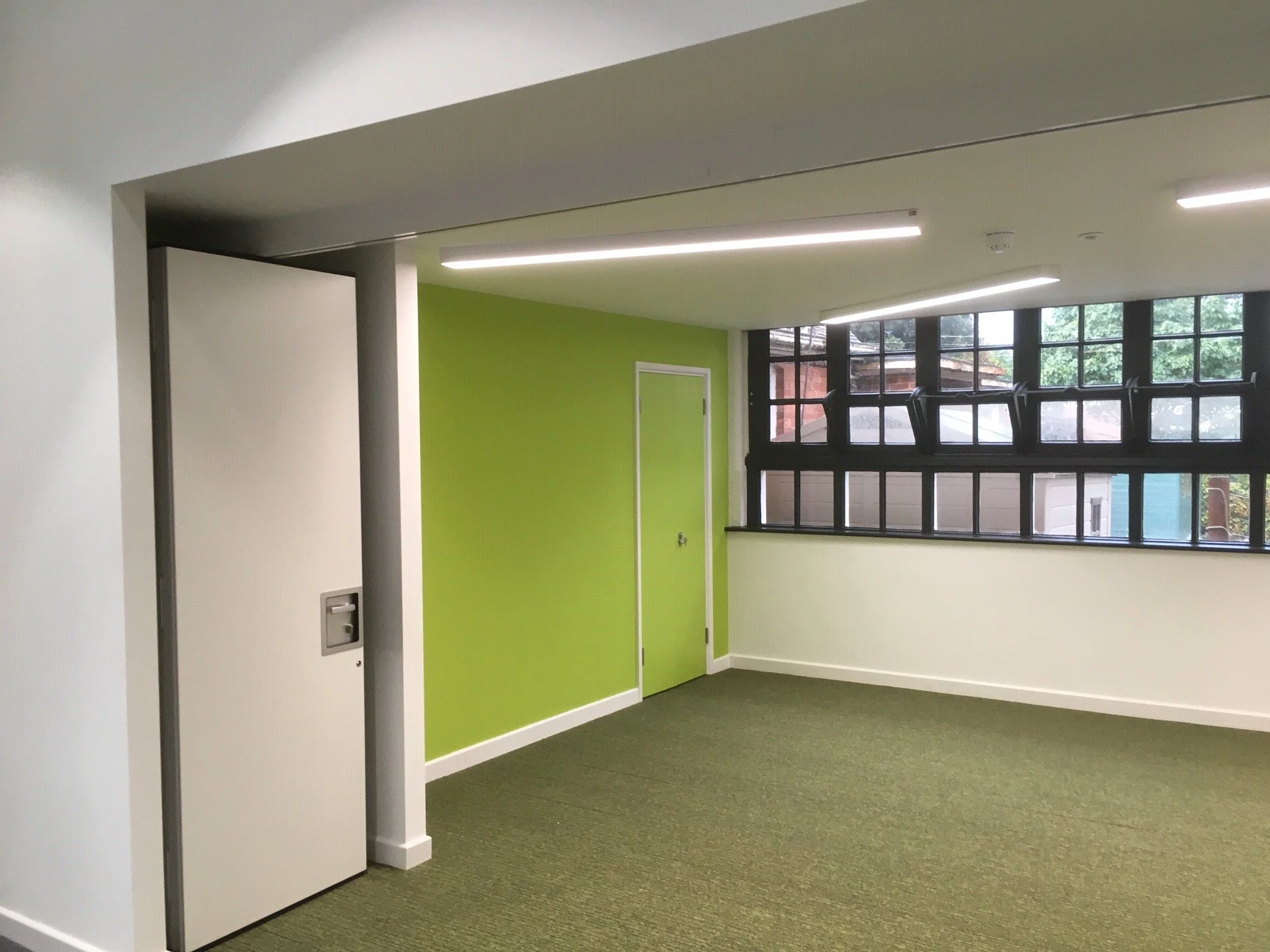Lime green painted classroom with moss coloured carpet and black framed windows.