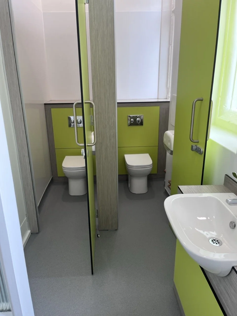 Lime green walled toilet area with two toilets and a white basin.