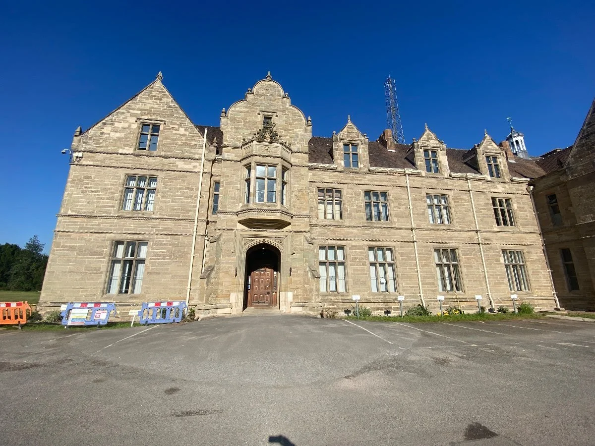 The front of a large two-story stone building with a large concrete driveway in front.