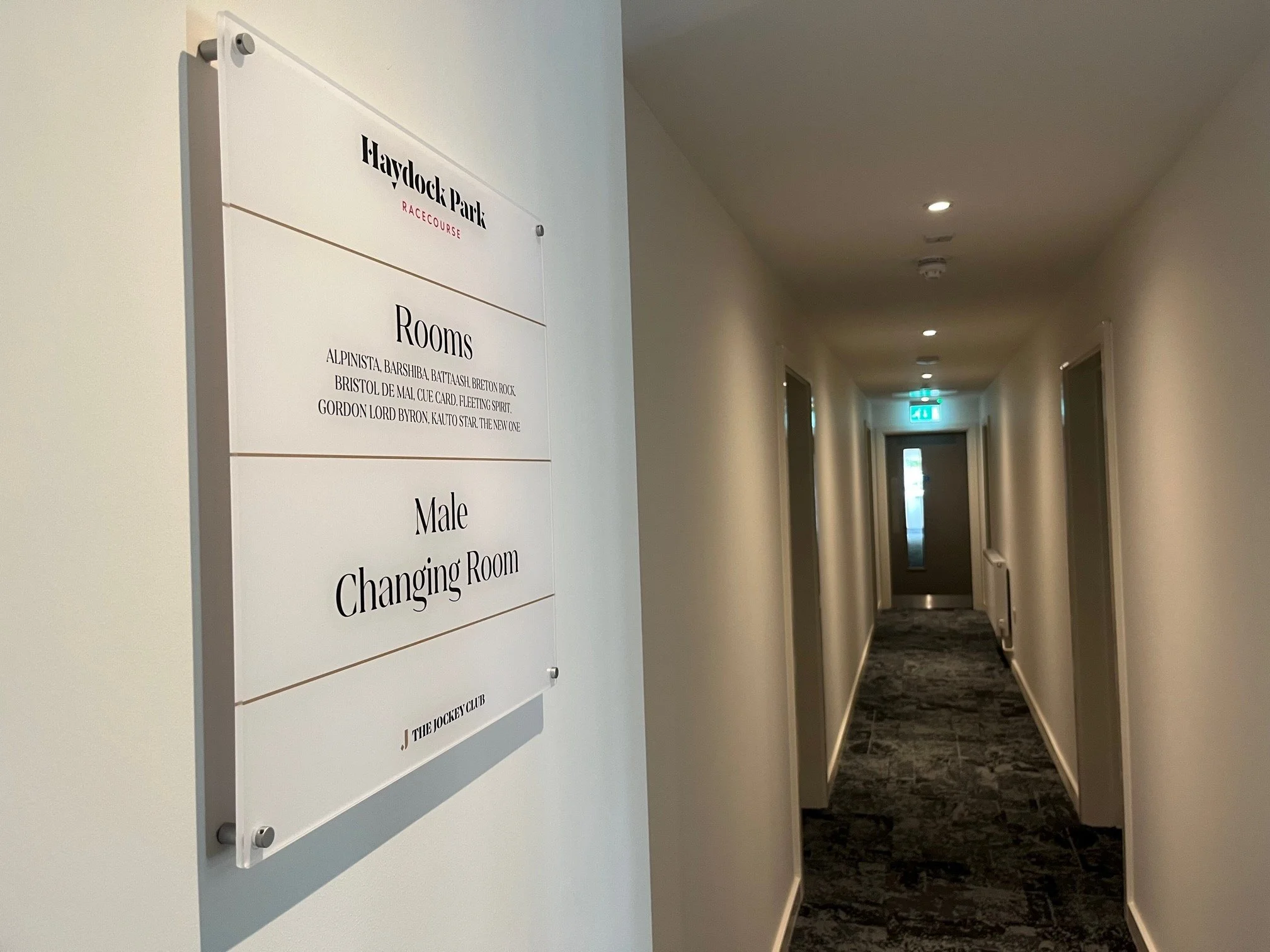 Long hotel corridor with a sign on the left hand side showing what facilities are available on each floor.
