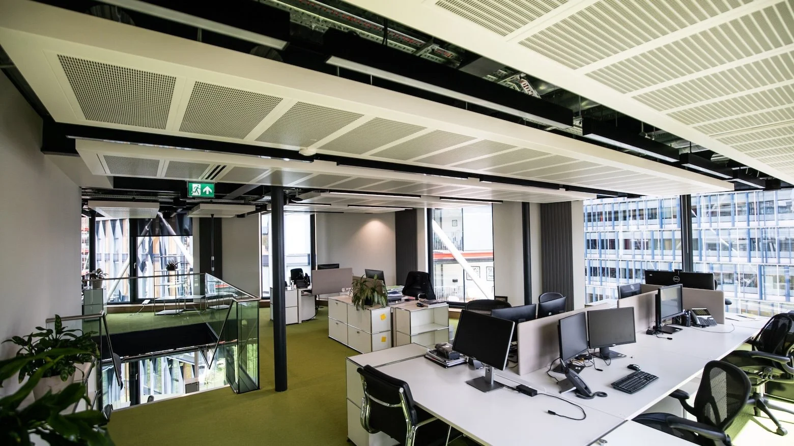 Large light-filled office space with green flooring and white desks. The external walls are floor-to-ceiling glass.