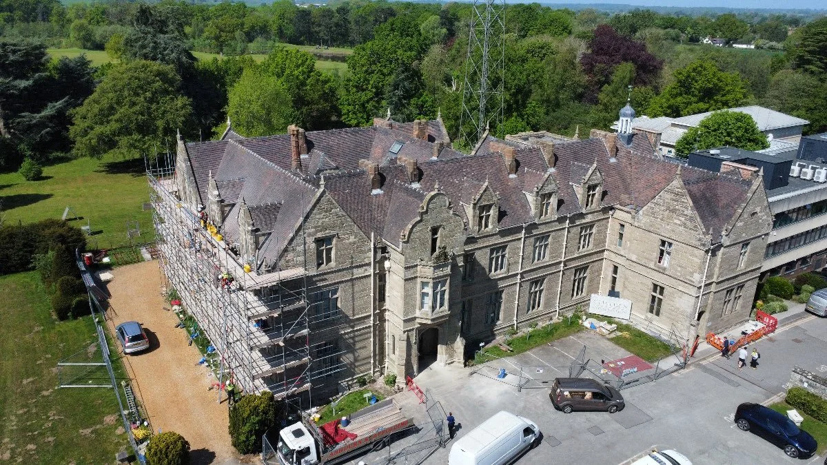 Overhead shot of a large stone two-story building with scaffolding on one side and trades vehicles outside the front.