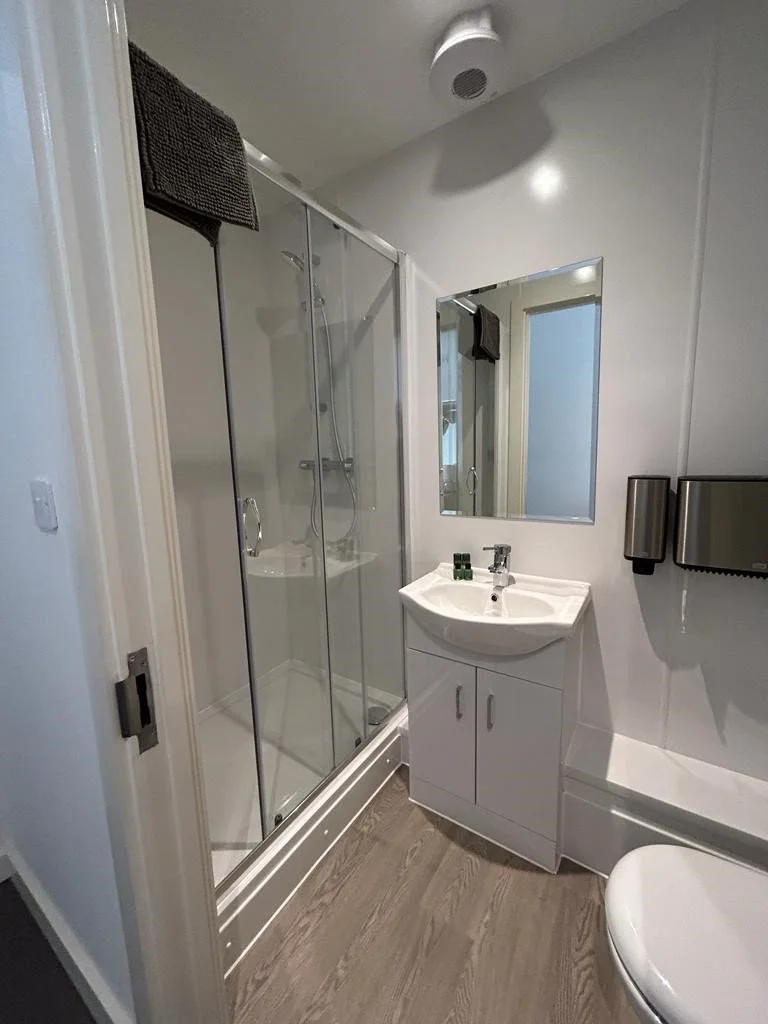 White hotel bathroom with a walk in shower and sink unit.
