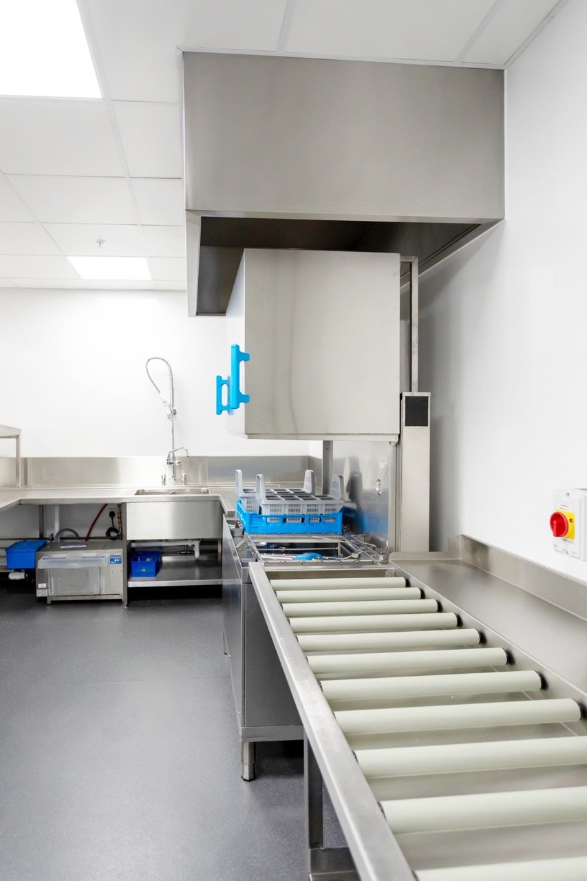 Glistening silver commercial kitchen a large industrial pot wash area with rollers sloping downwards for trays of clean items.
