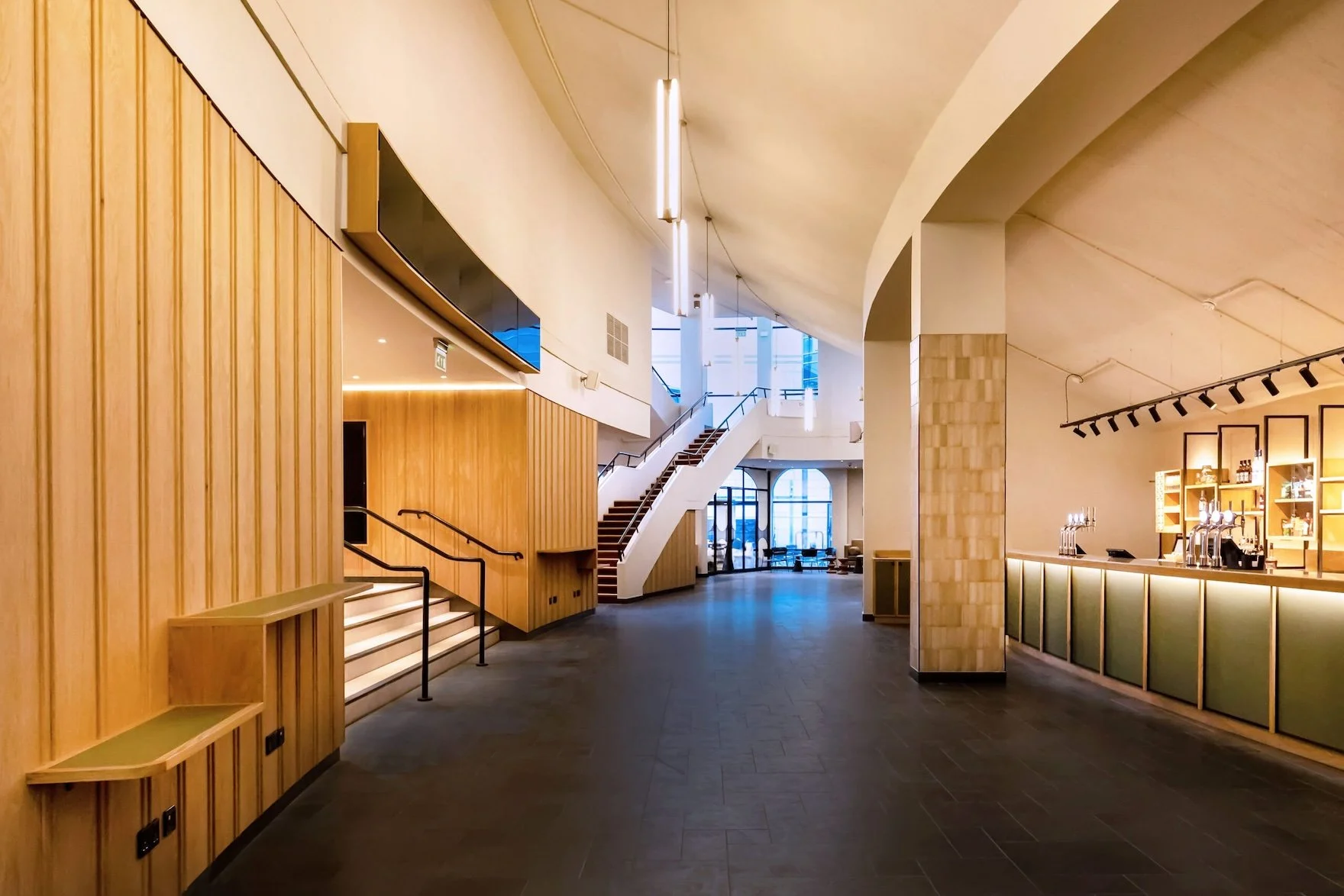 Large, empty leisure venue with a bottle green-fronted bar running along one side and a wide, beige staircase with black handrails on the other.